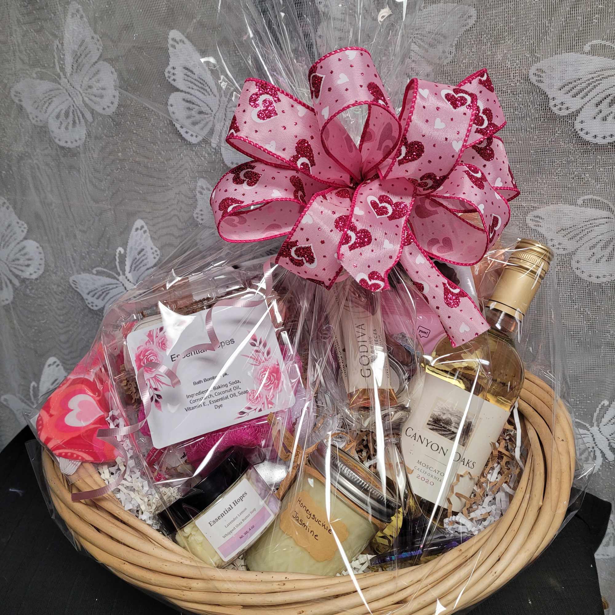 Gift basket with bath and body items wrapped in clear cellophane and topped with a pink heart ribbon