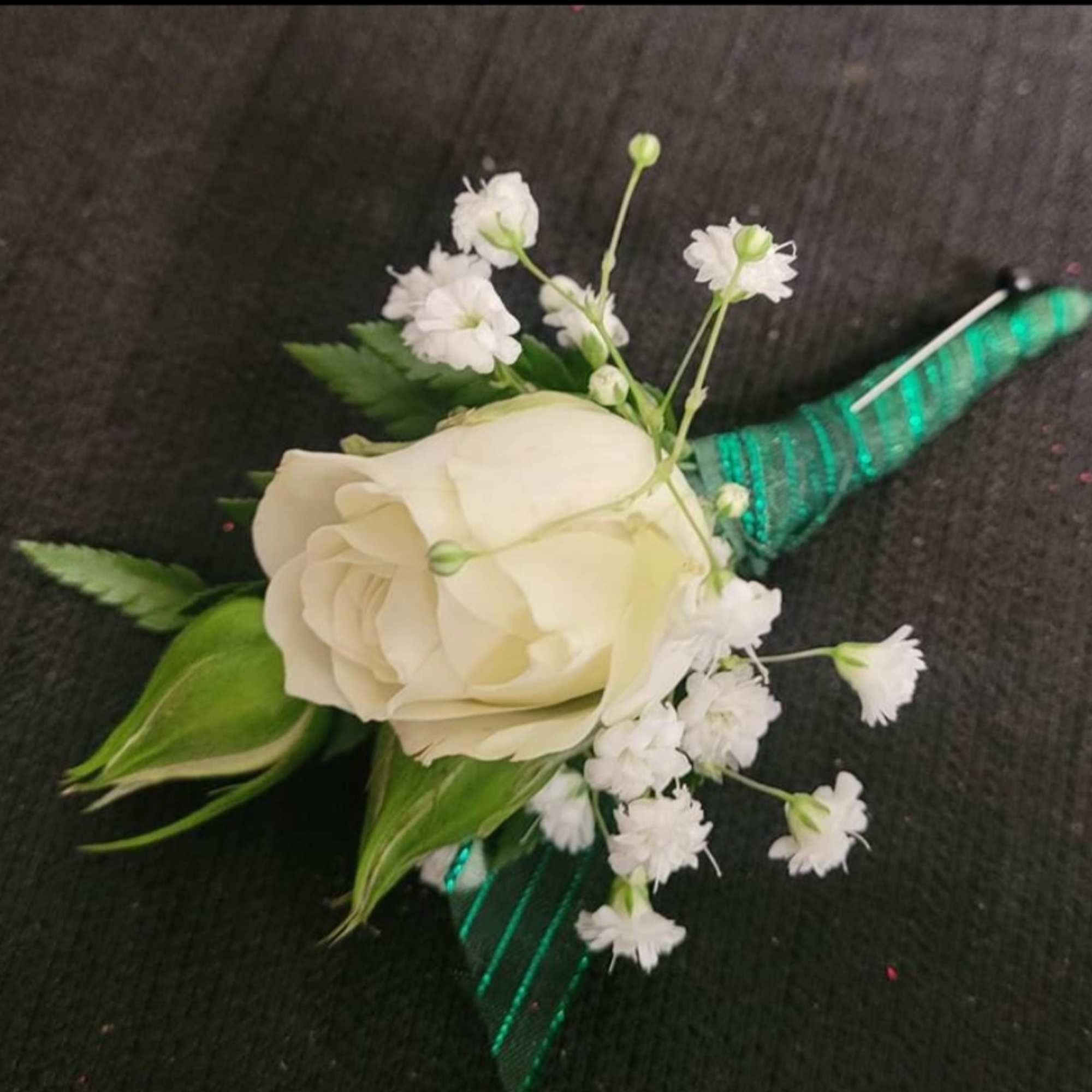 White rose boutonniere with baby's breath and green ribbon wrap