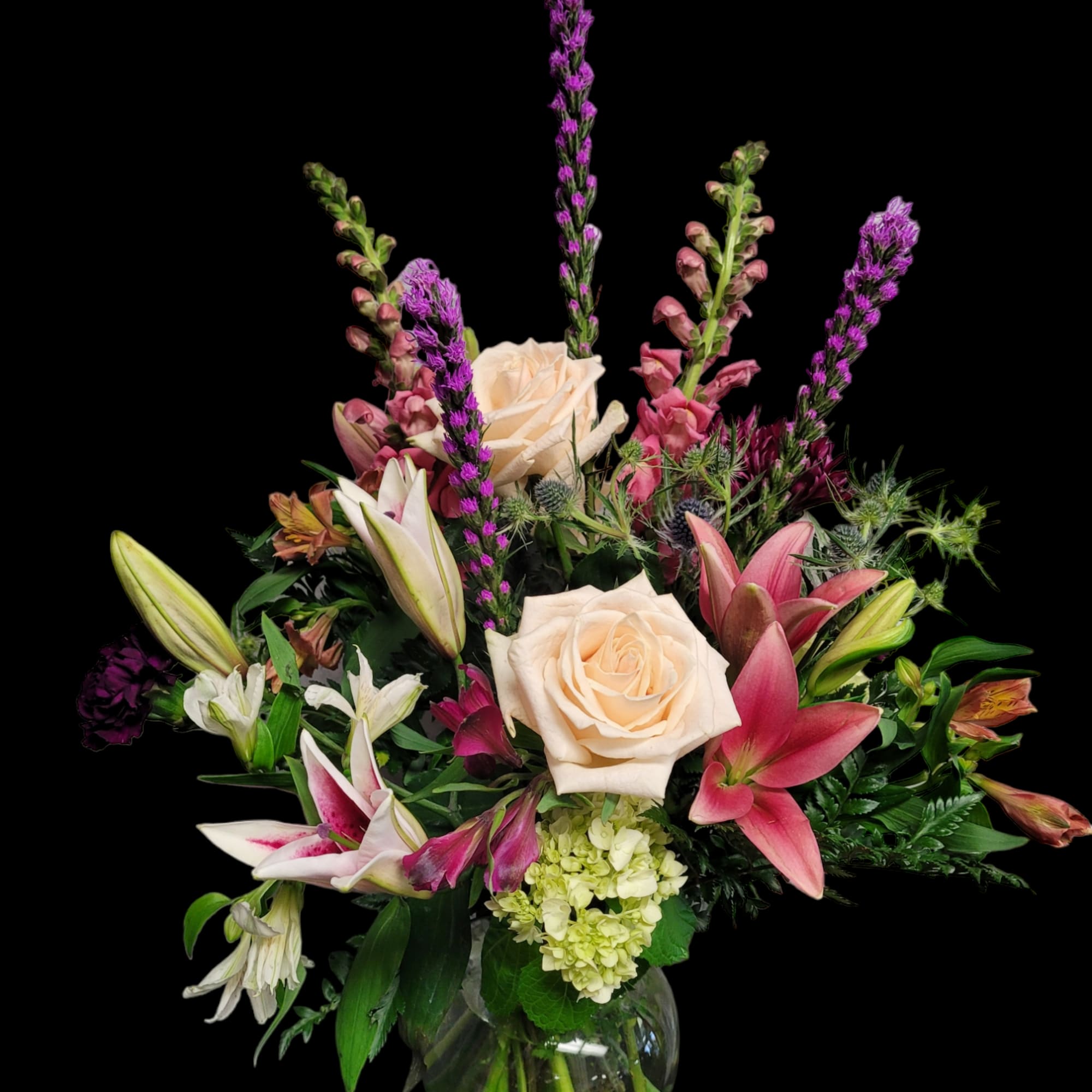 Mixed bouquet of roses, lilies, and purple spikes in a glass vase