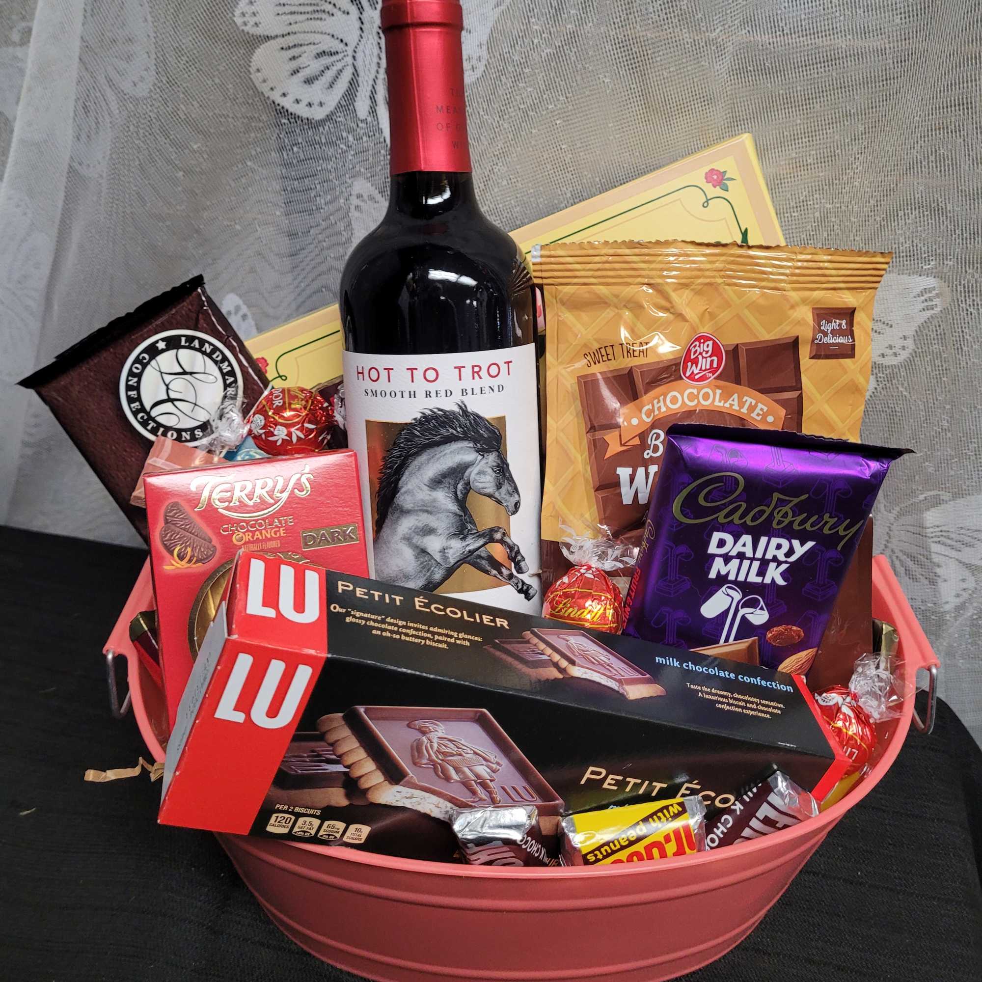 Gift basket with a wine bottle, chocolates, and cookies in a pink tray