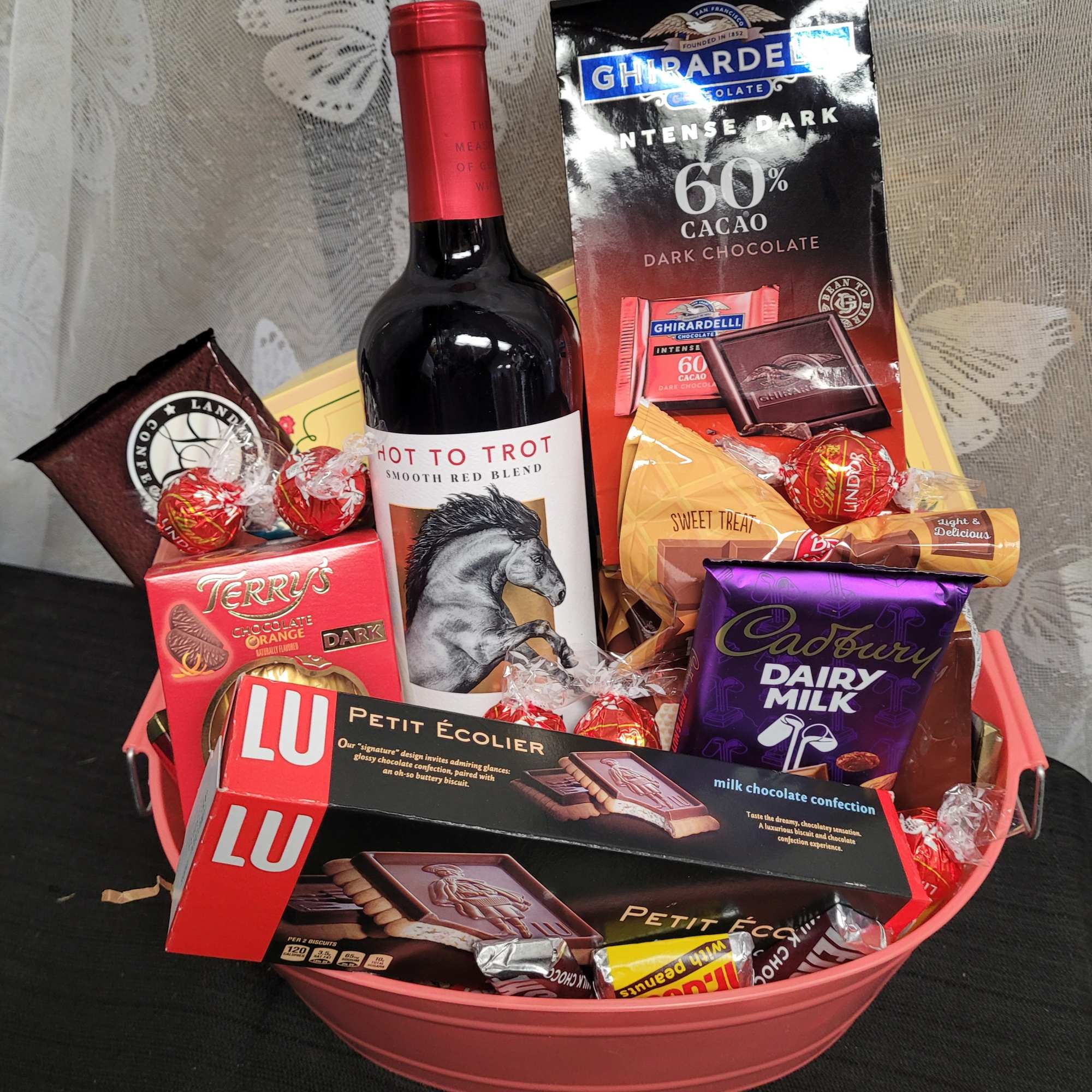 Gift basket with wine, chocolates, and candy in a pink tub