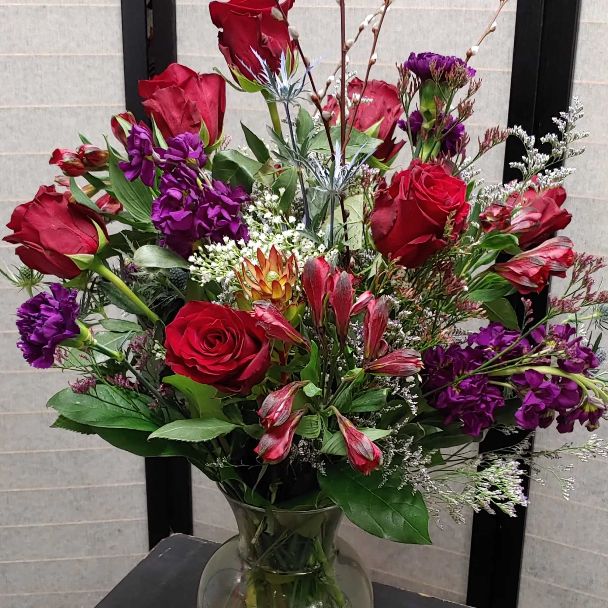Mixed bouquet of red roses and purple flowers in a glass vase