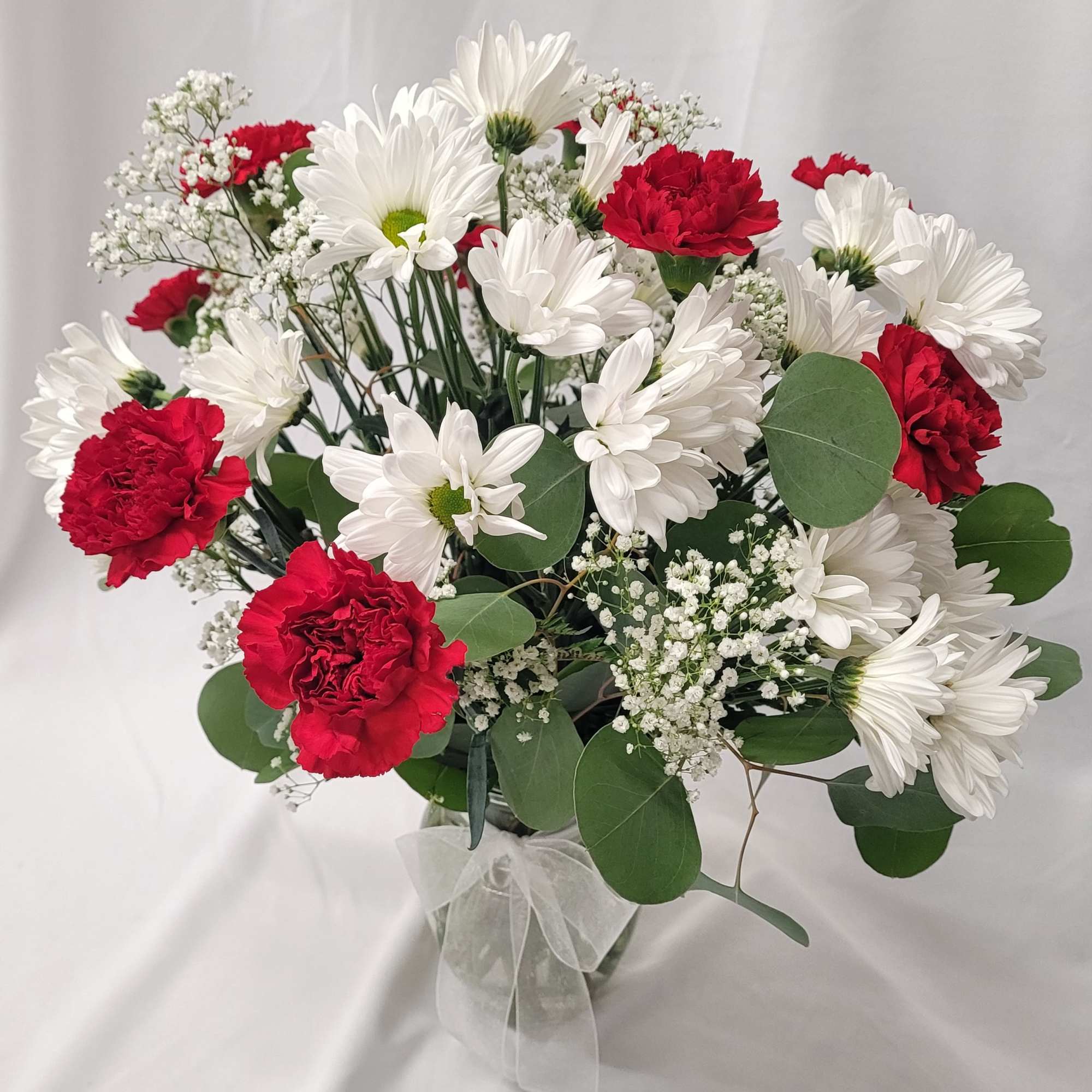 Bouquet of white daisies and red carnations in a clear vase with a white ribbon