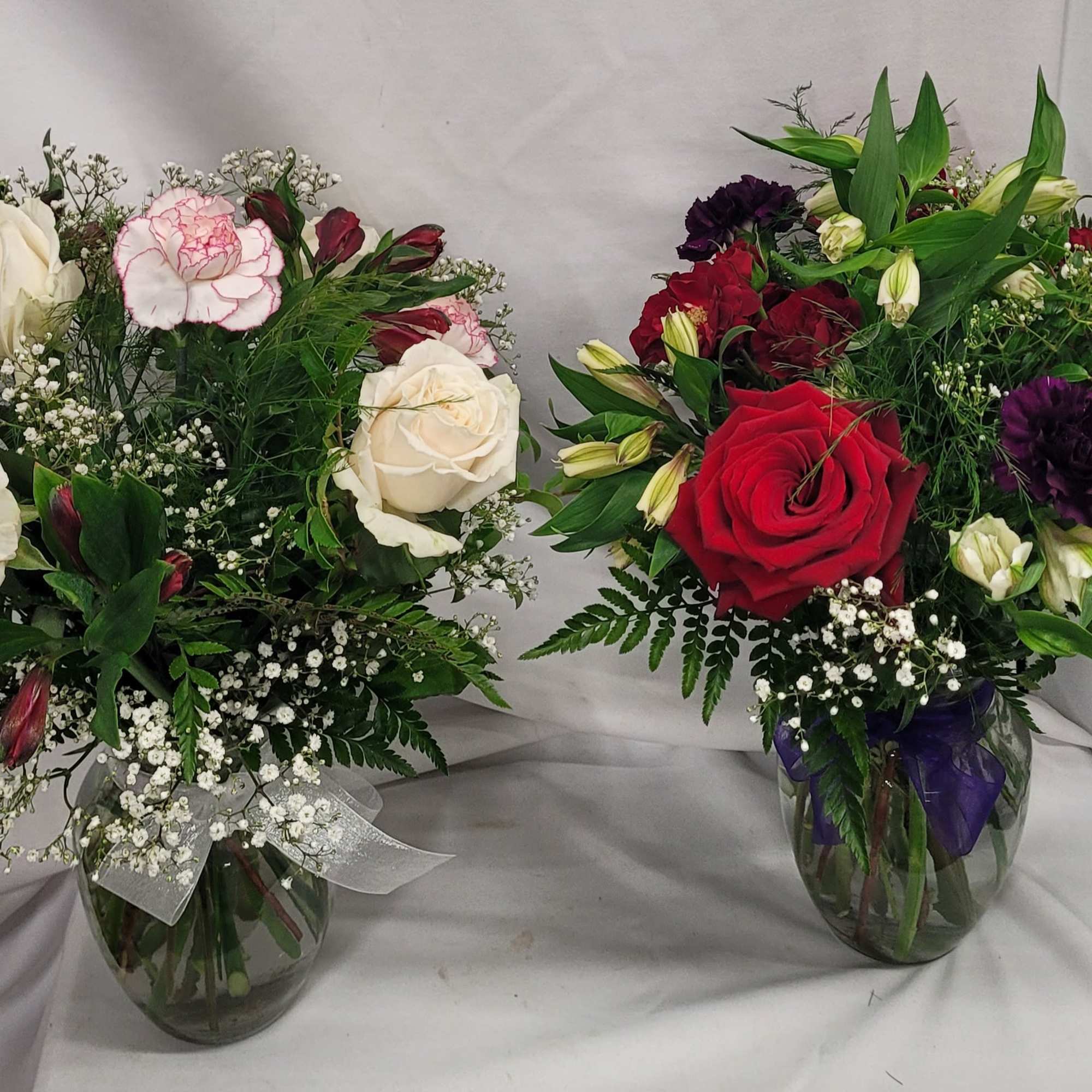 Two mixed rose bouquets in glass vases, one red and one white with pink accents.