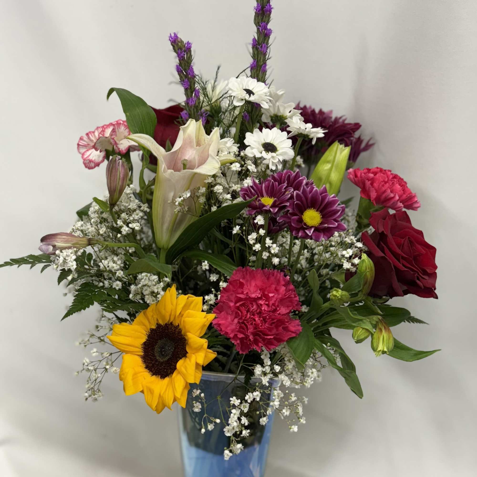 Mixed bouquet in a blue glass vase with sunflower, roses, lilies, and daisies
