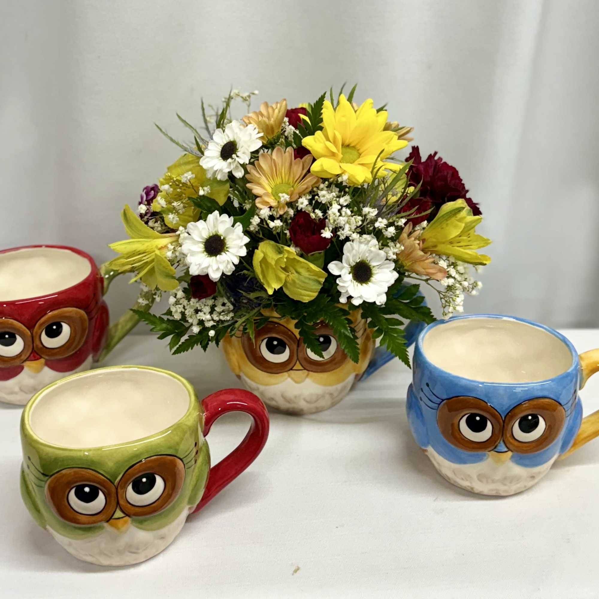Mixed flower bouquet in an owl-shaped mug surrounded by three owl mugs