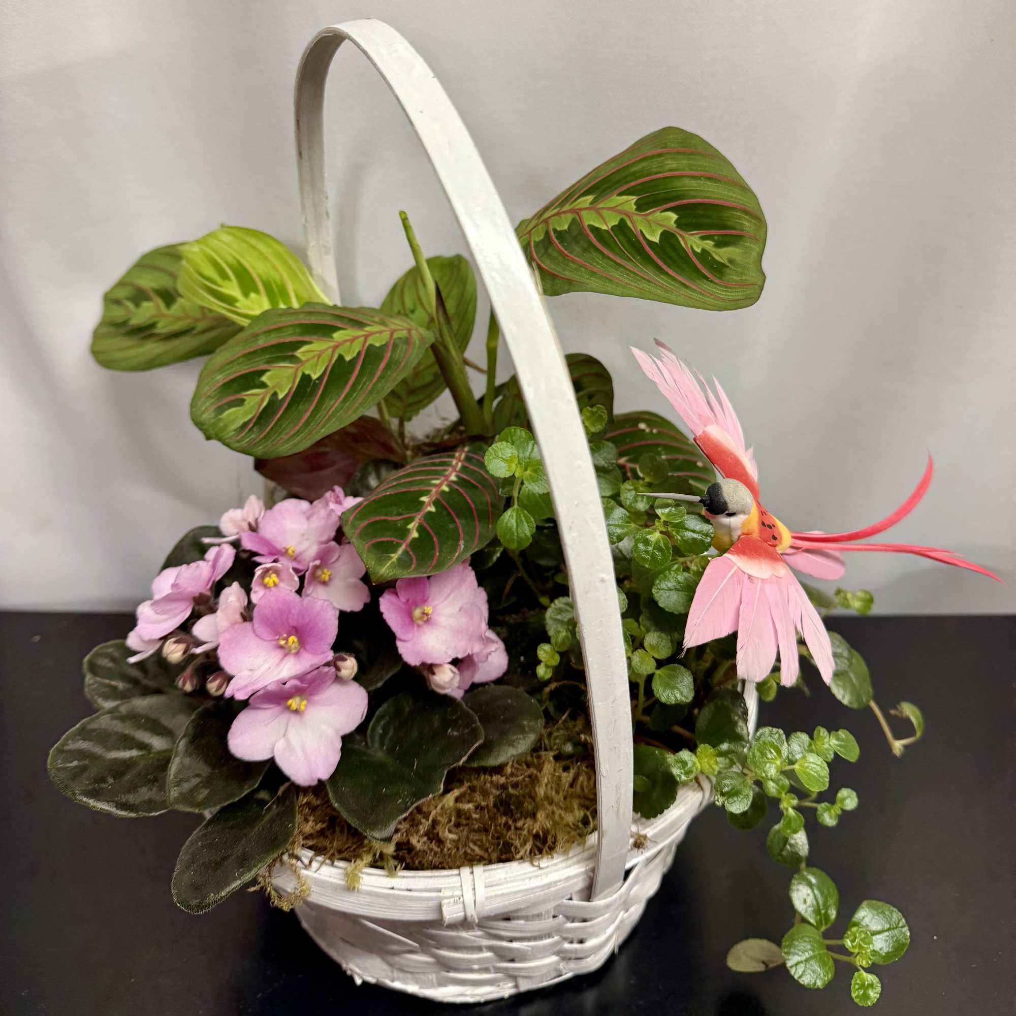Basket planter with pink violets, striped leaves, and a pink bird decoration