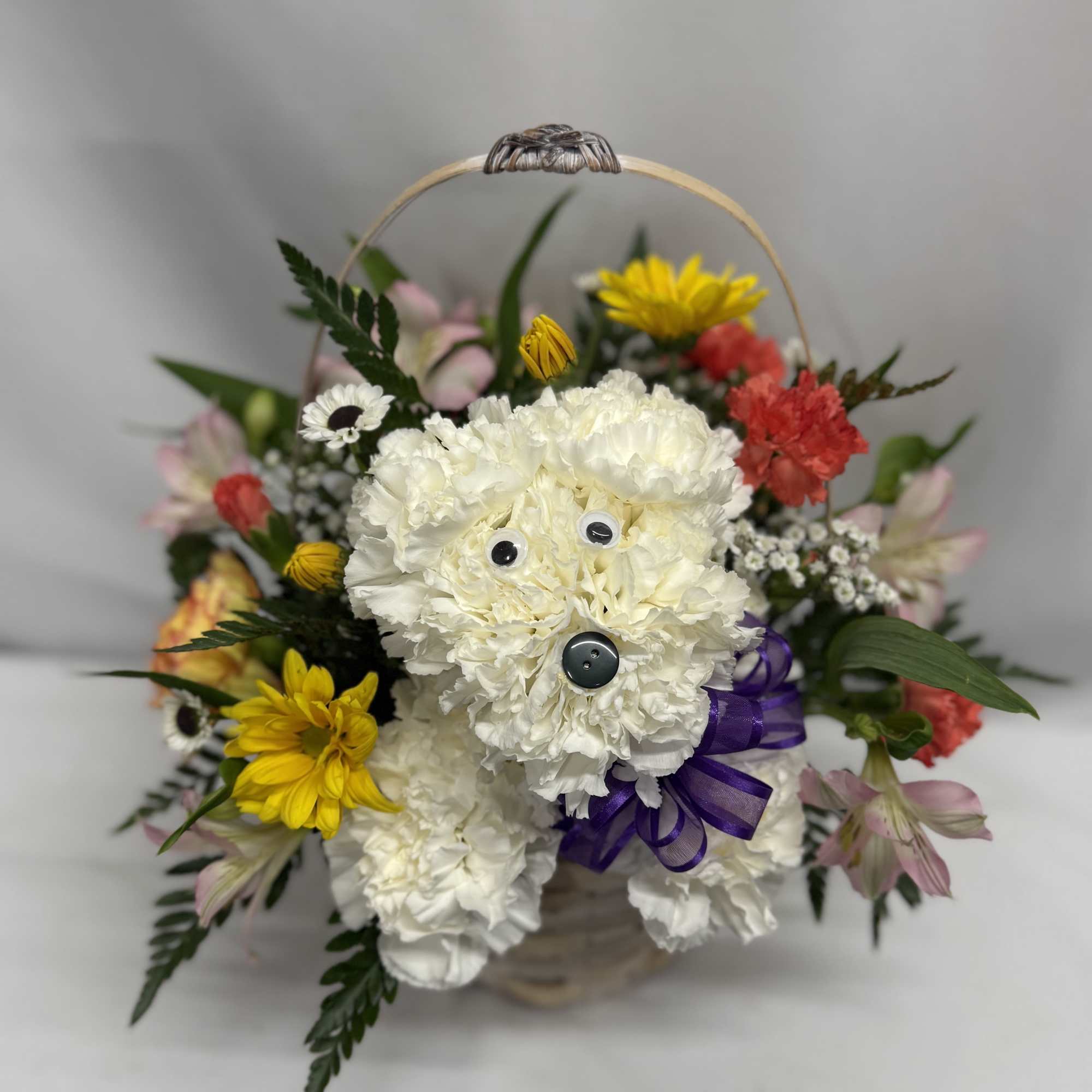 Basket arrangement with a white carnation dog figure surrounded by mixed yellow and pink flowers.