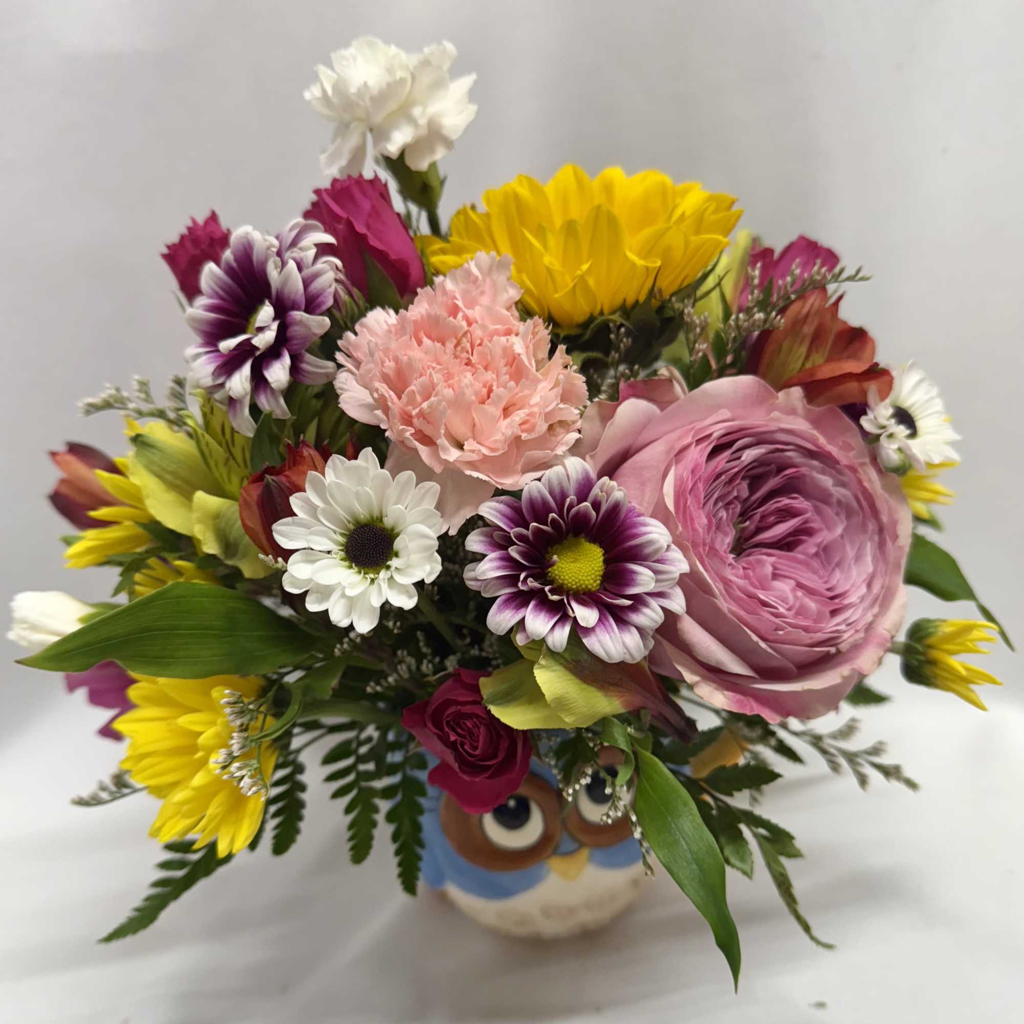 Mixed bouquet in an owl vase with pink, yellow, white, and purple flowers