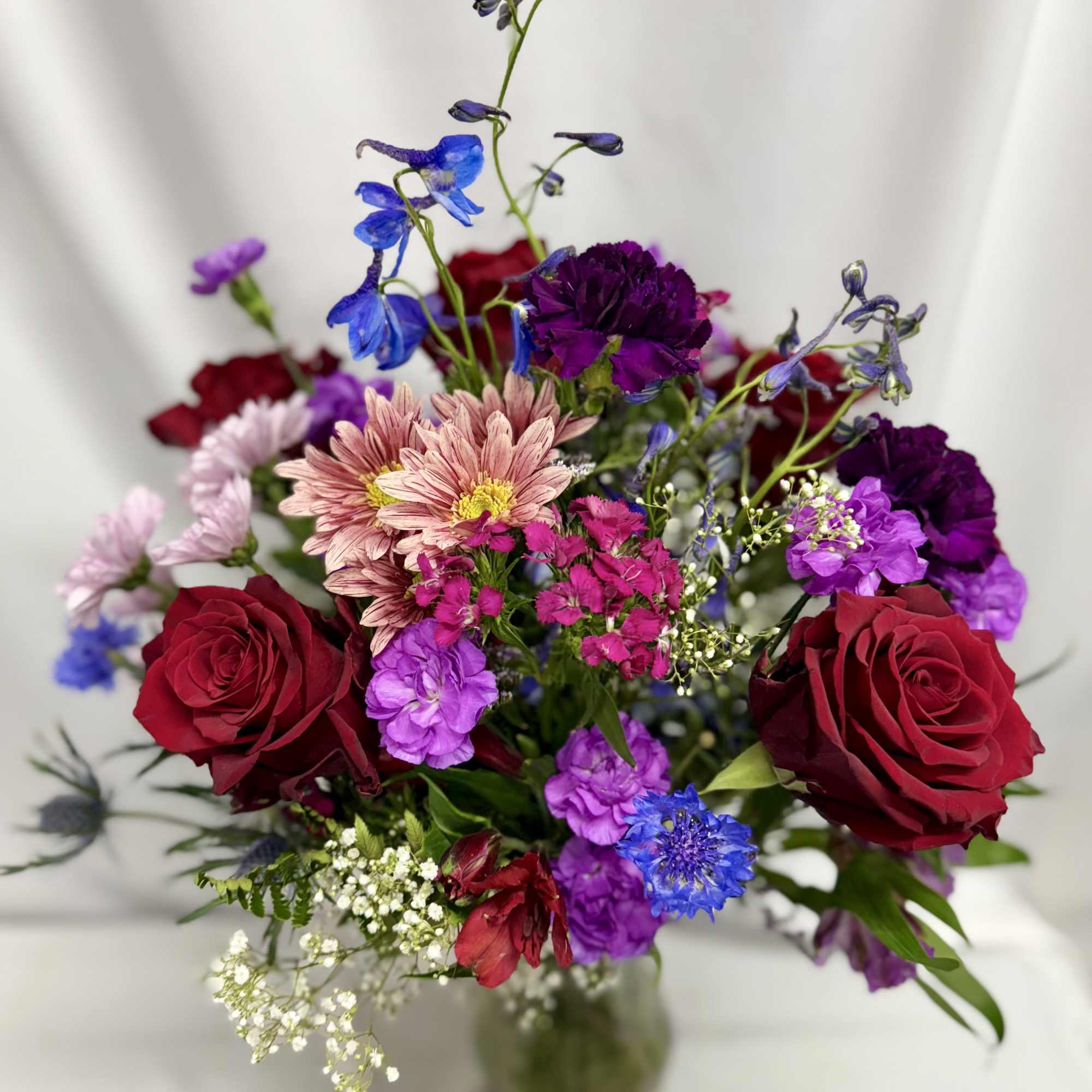 Mixed bouquet of red roses, purple blooms, and pink daisies in a glass vase