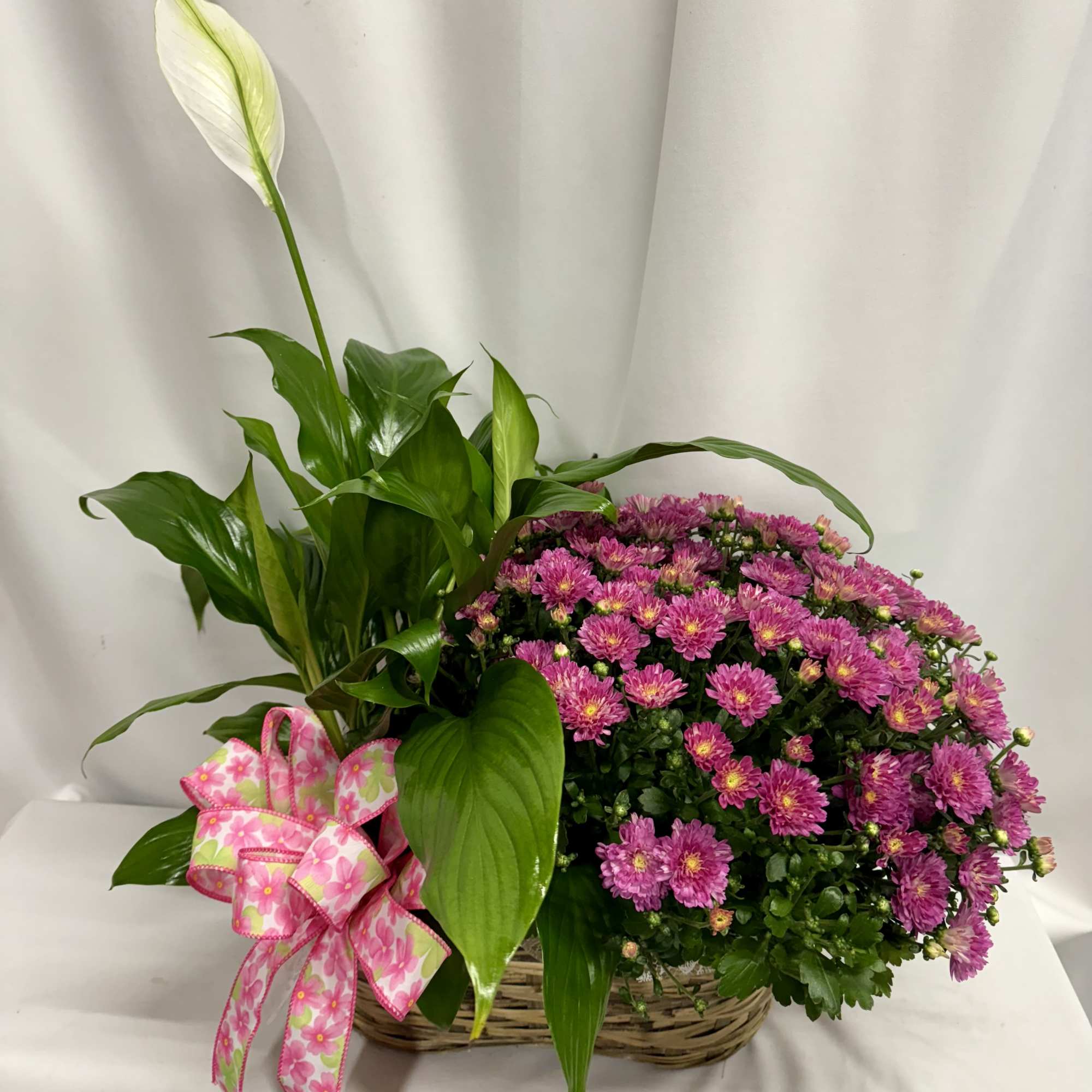 Basket arrangement with pink chrysanthemums and a white peace lily bloom