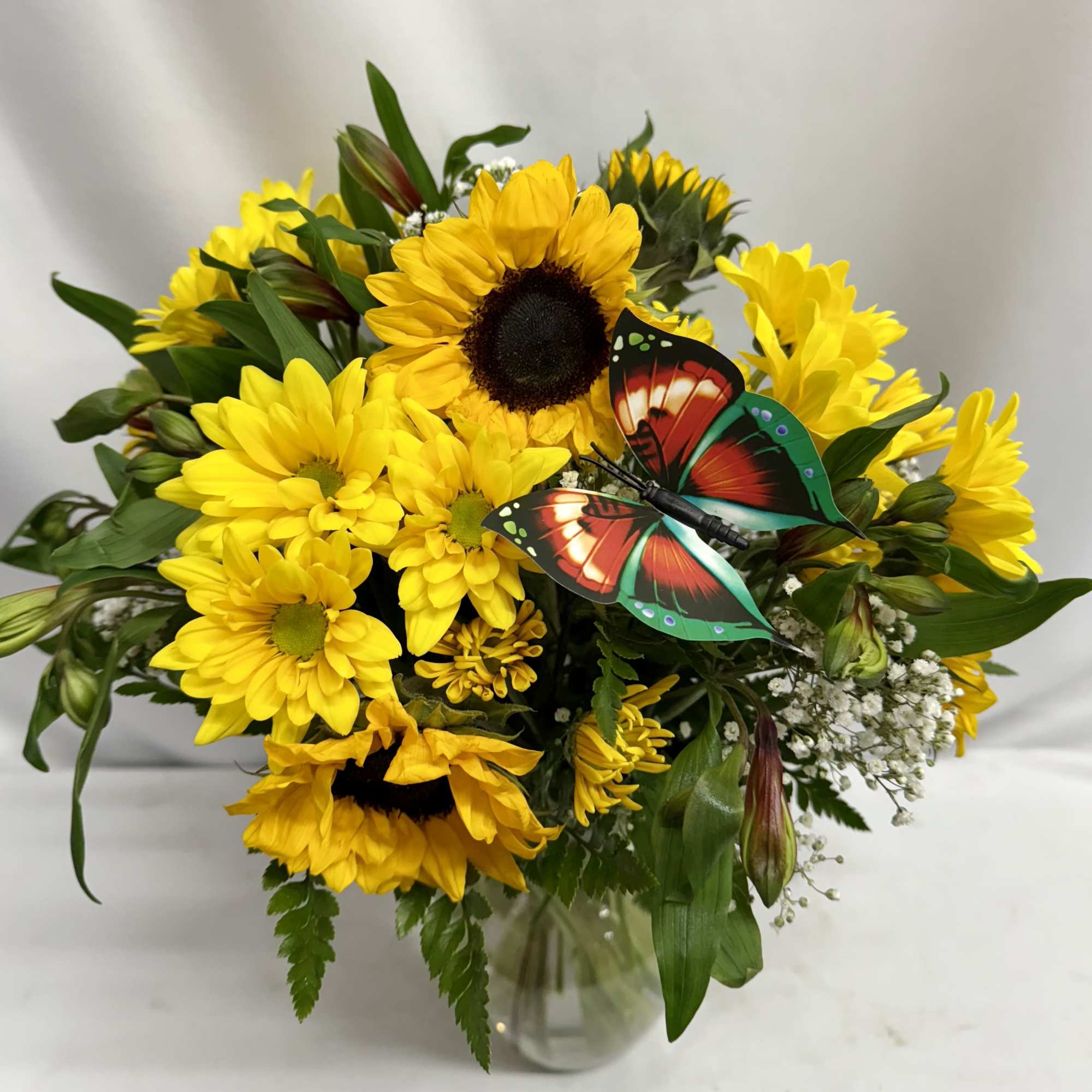 Yellow sunflower and daisy bouquet in a glass vase with a butterfly decoration