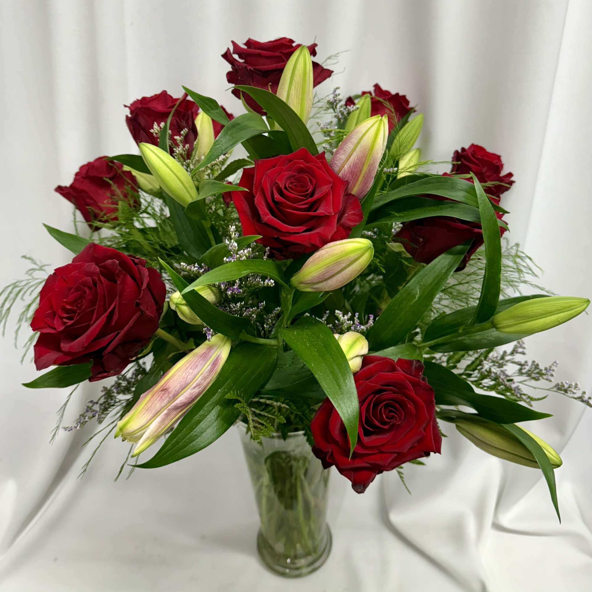Red roses and lily buds arranged in a clear glass vase