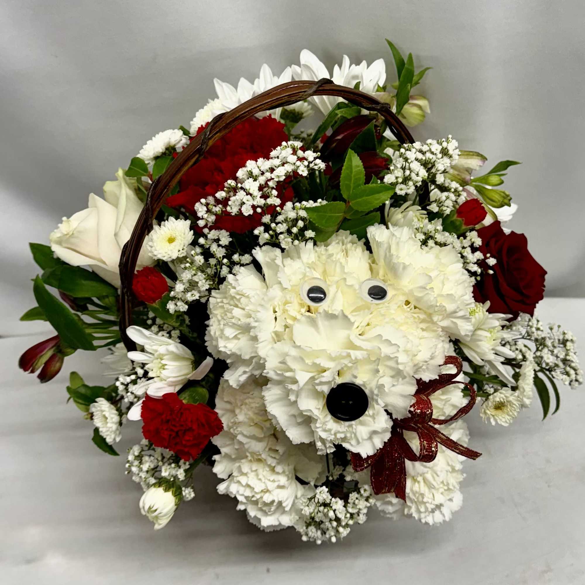 Basket arrangement with white carnation dog figure, red roses, red carnations, and white daisies