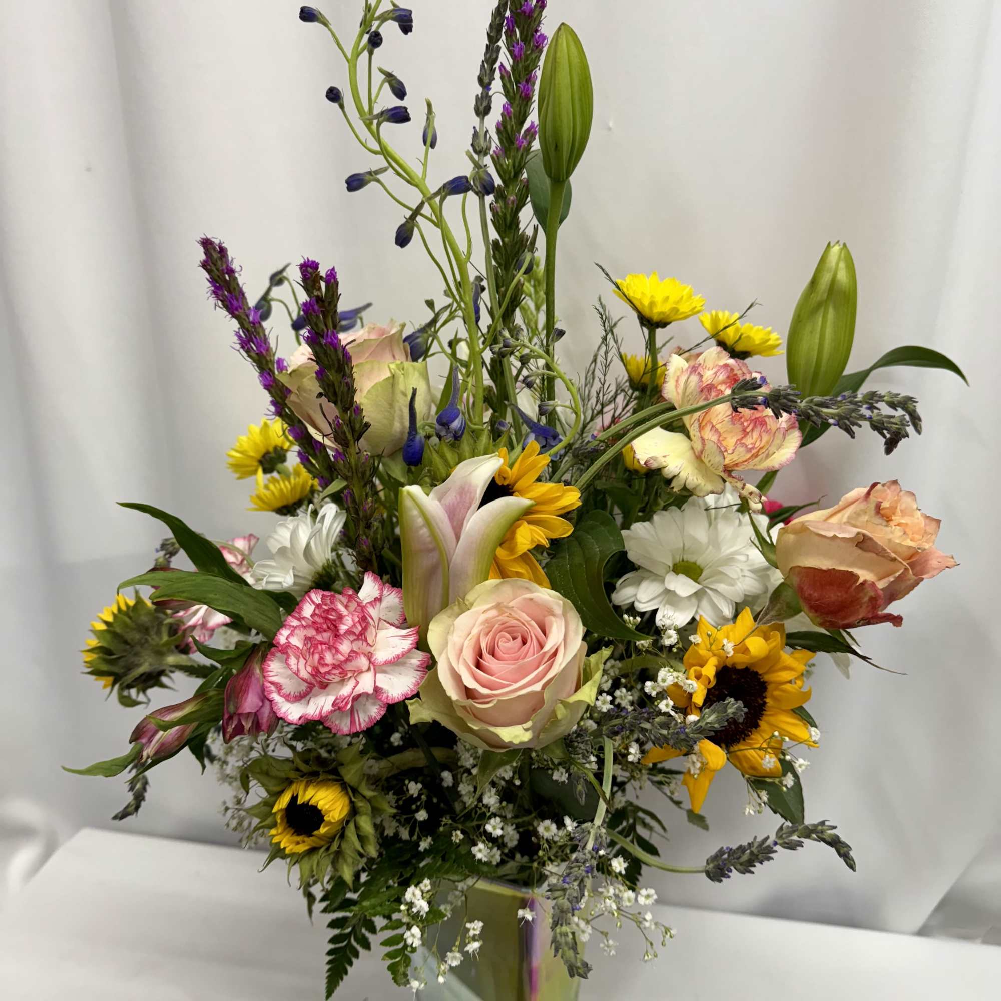 Mixed bouquet of roses, lilies, sunflowers, and daisies in a glass vase