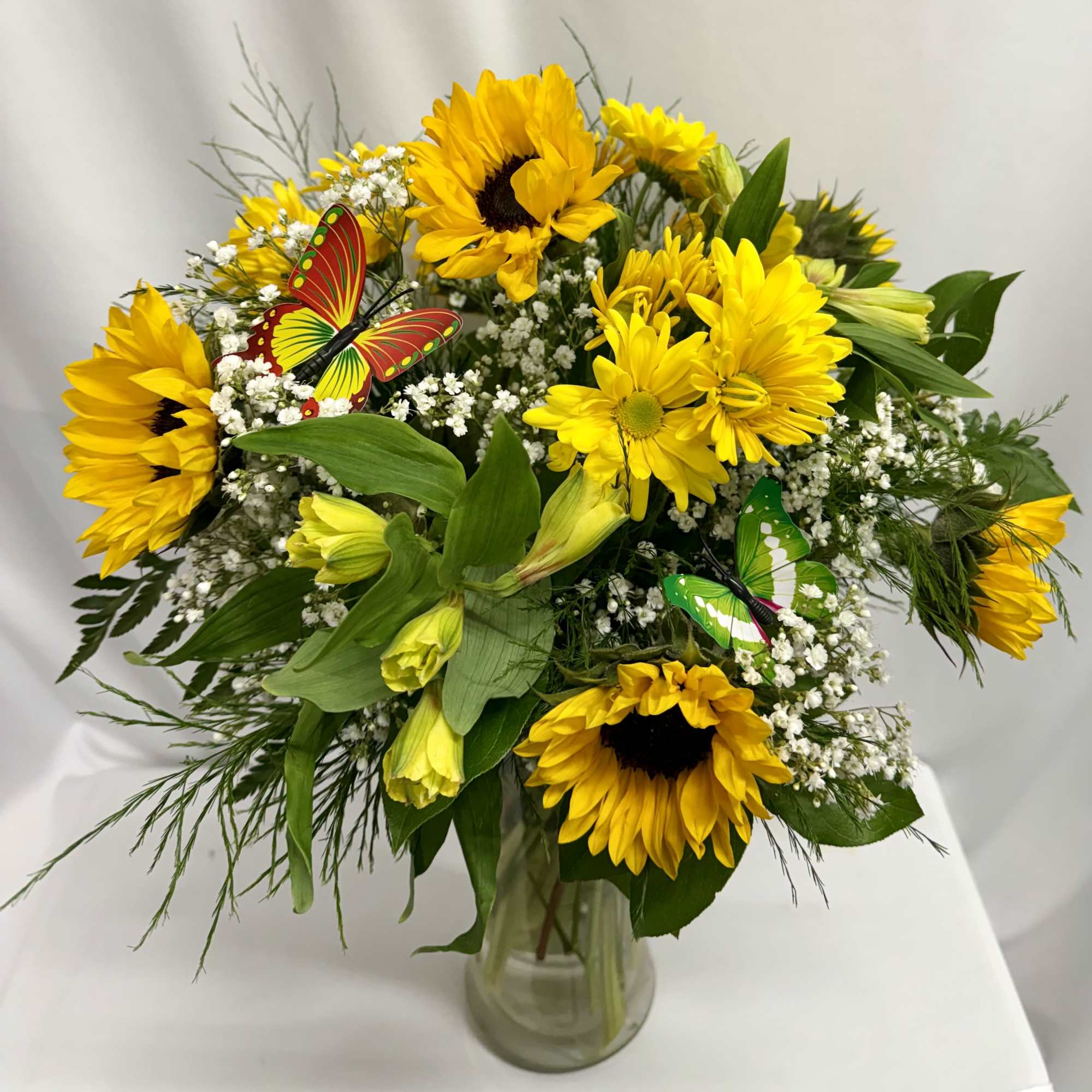 Yellow sunflower bouquet in a glass vase with butterfly picks