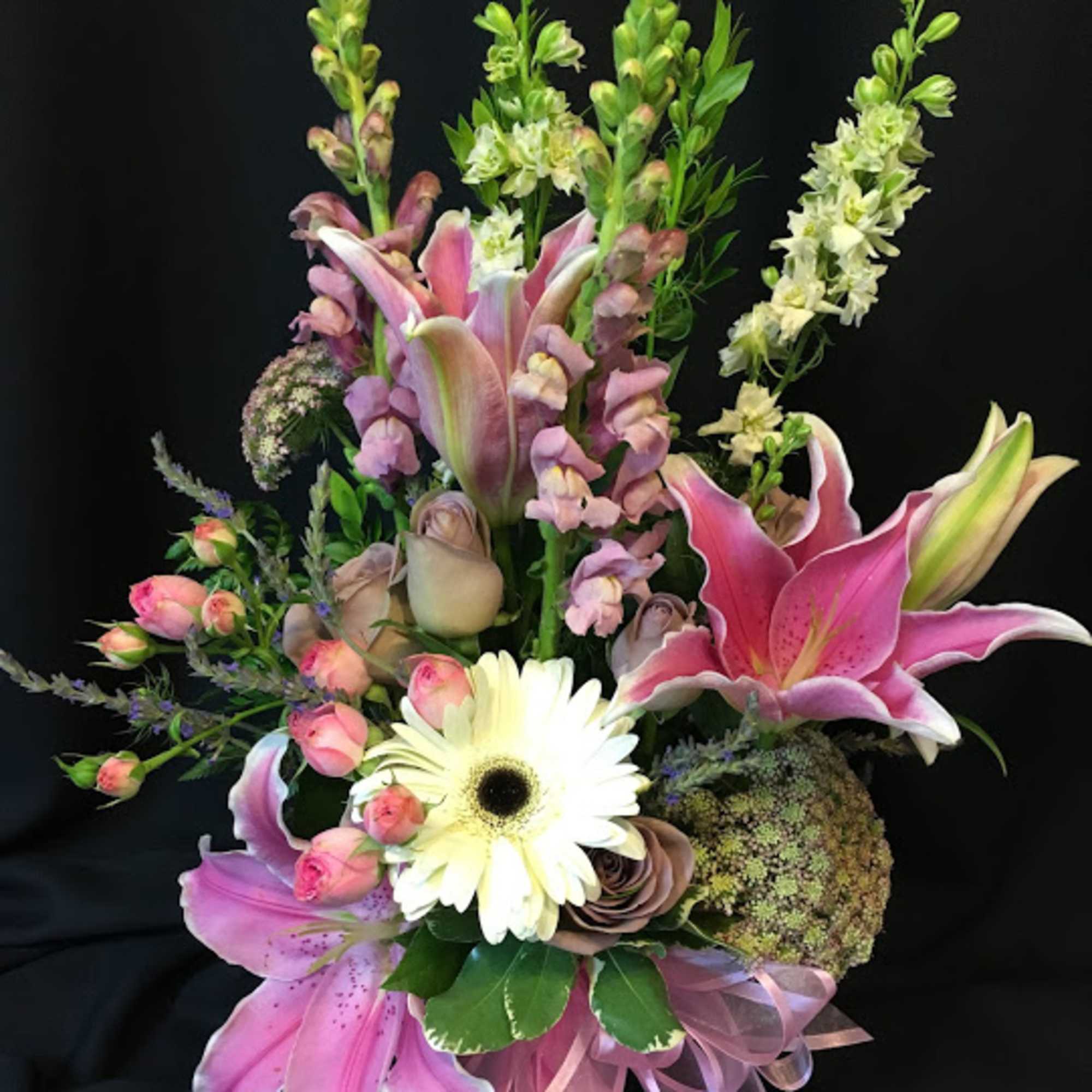 Pink lilies and mixed blooms arranged in a vase with a ribbon bow