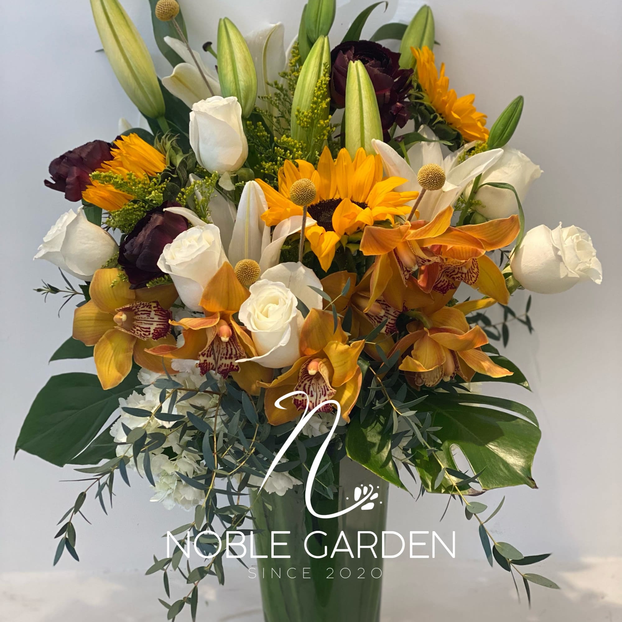 Mixed bouquet of lilies, roses, orchids, and sunflowers in a glass vase