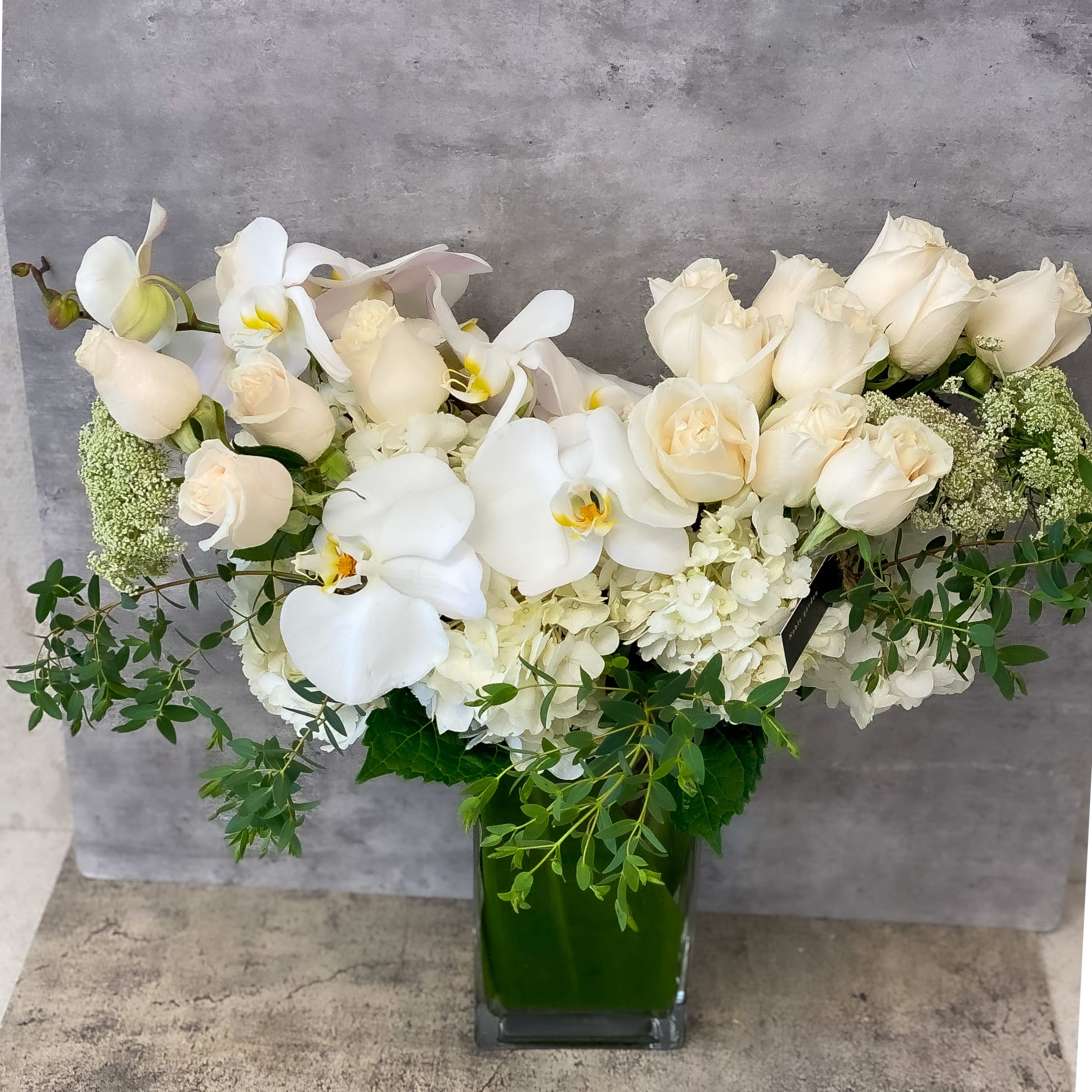 White roses and orchids arranged in a green glass vase