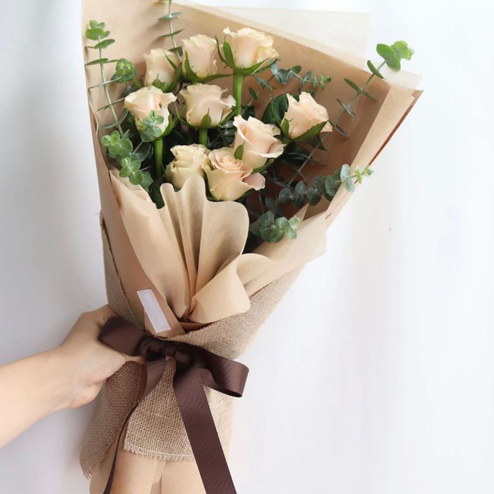Bouquet of pale peach roses wrapped in brown paper with a ribbon