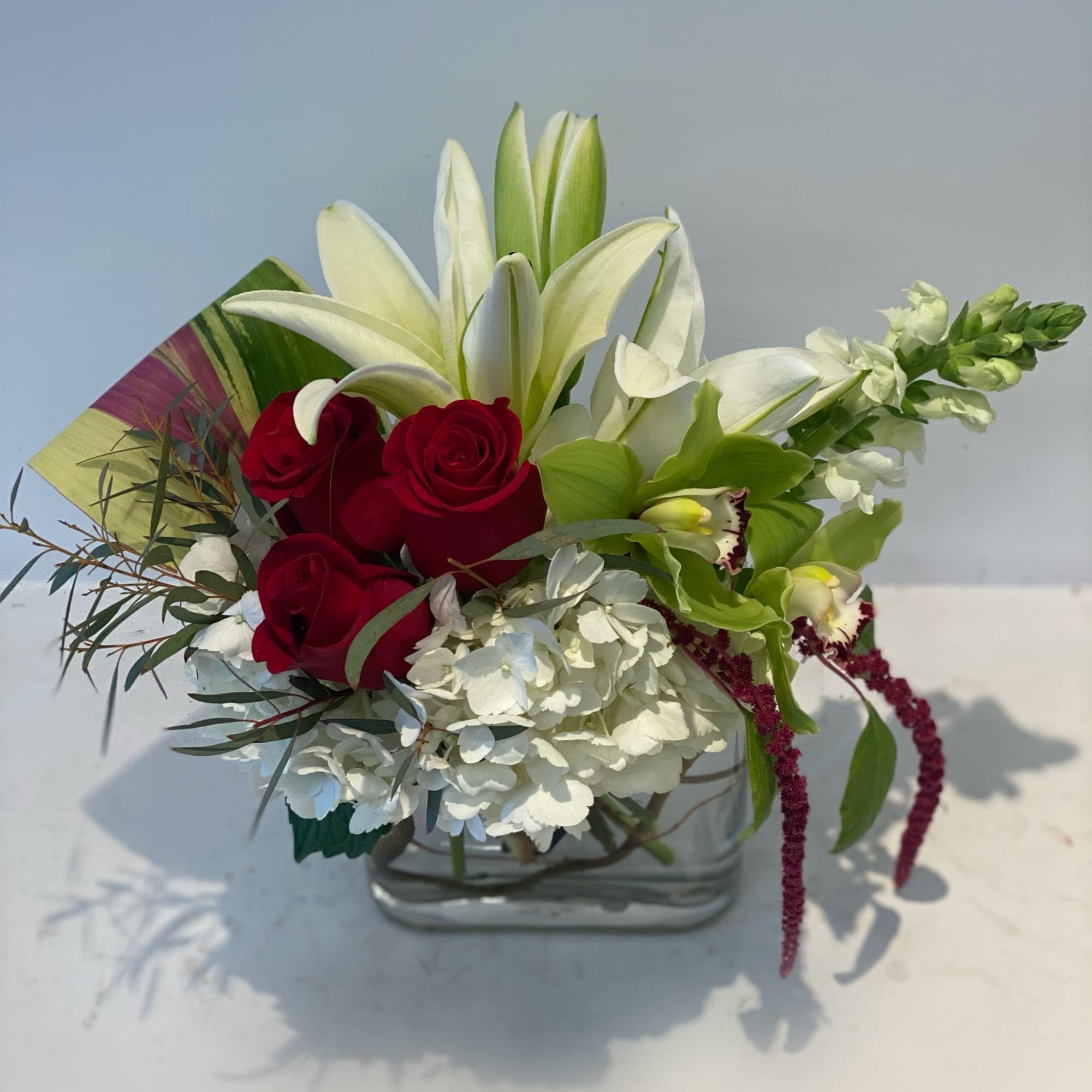 Red roses and white lilies in a clear glass vase with white hydrangea