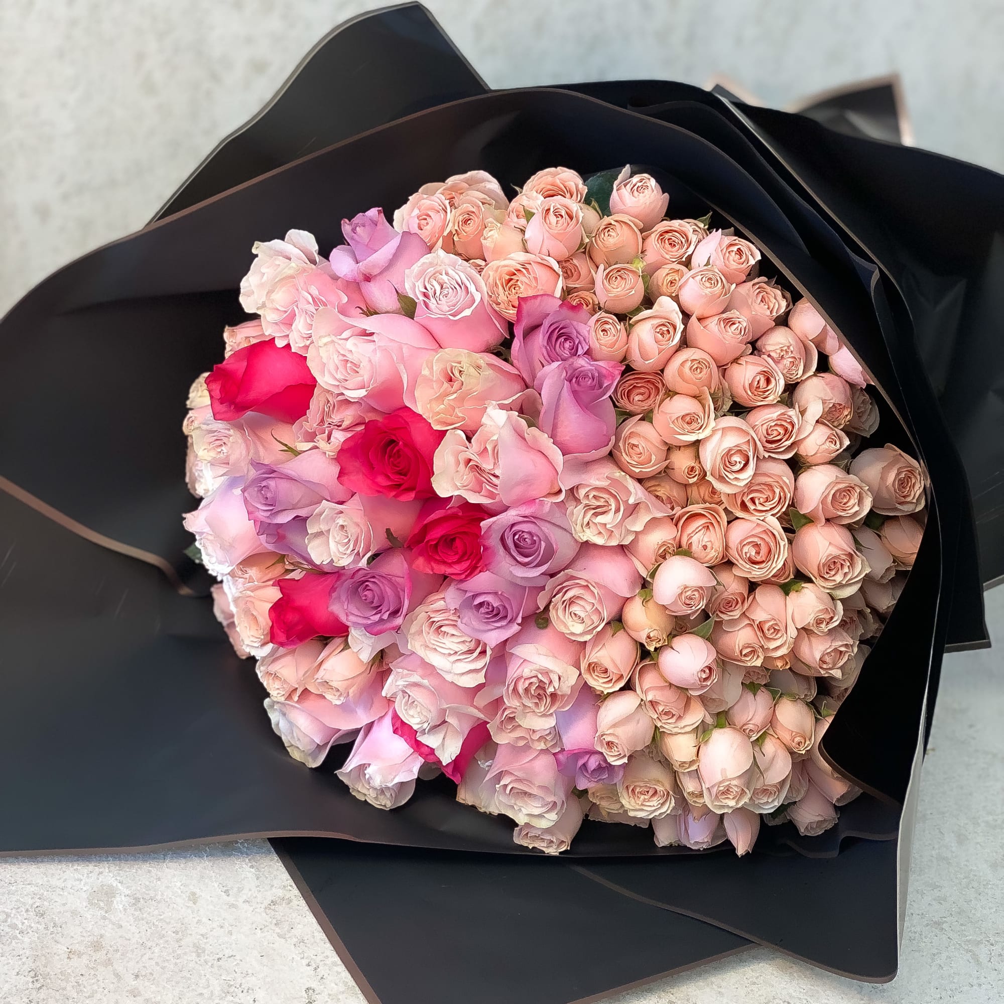 Large bouquet of pink and lavender roses wrapped in black paper