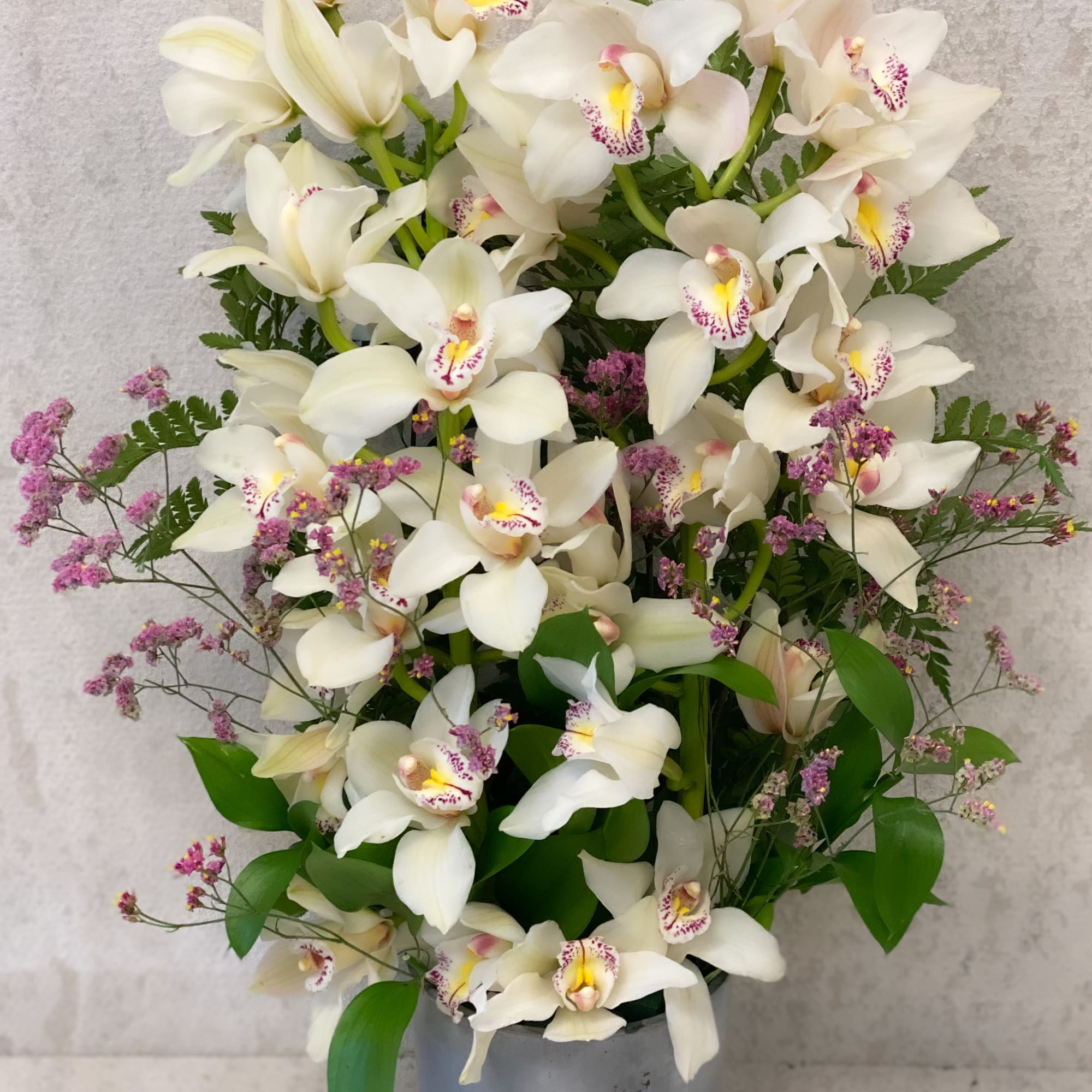 White orchids arranged in a gray pot with small purple filler flowers