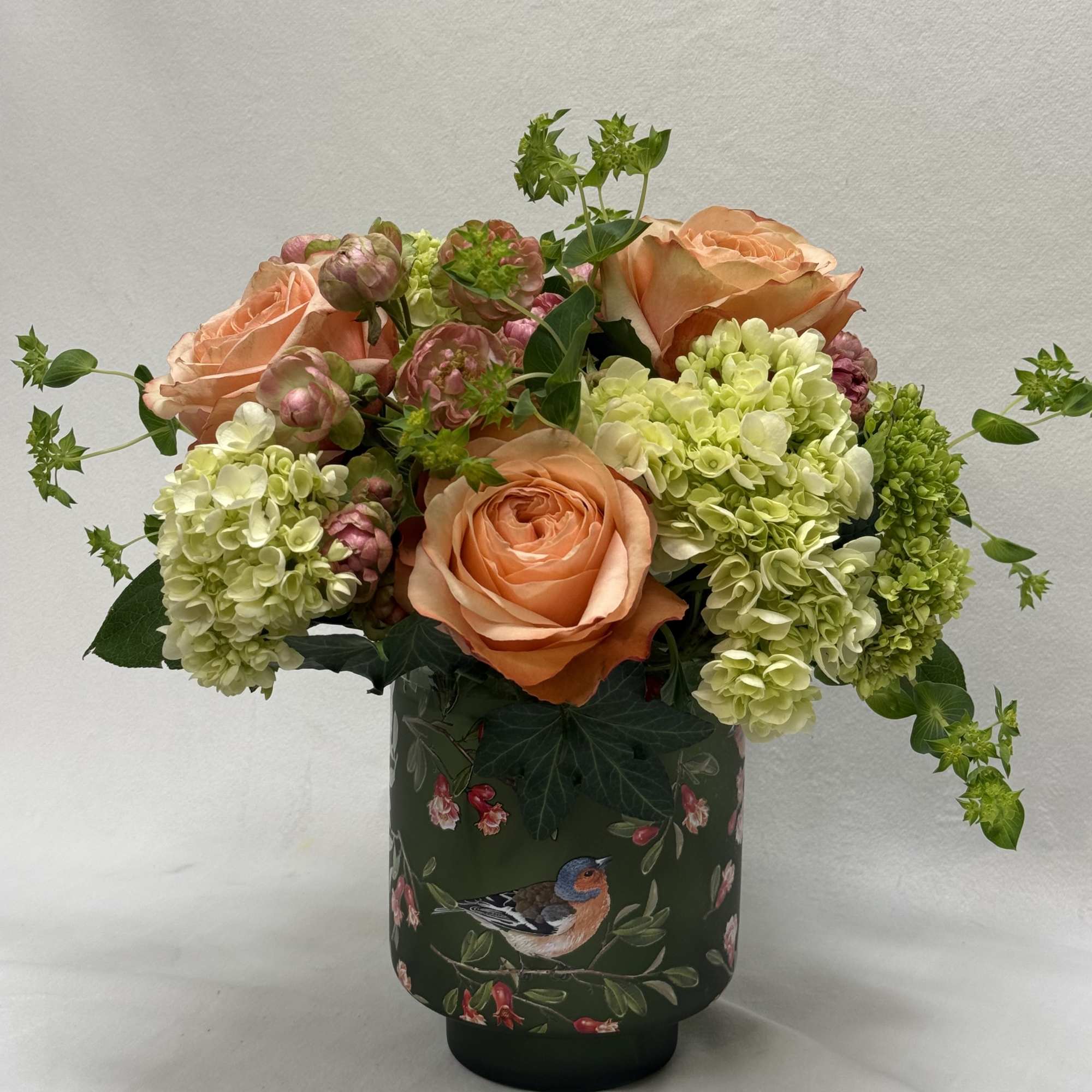 Peach roses and pale green hydrangeas in a decorative vase
