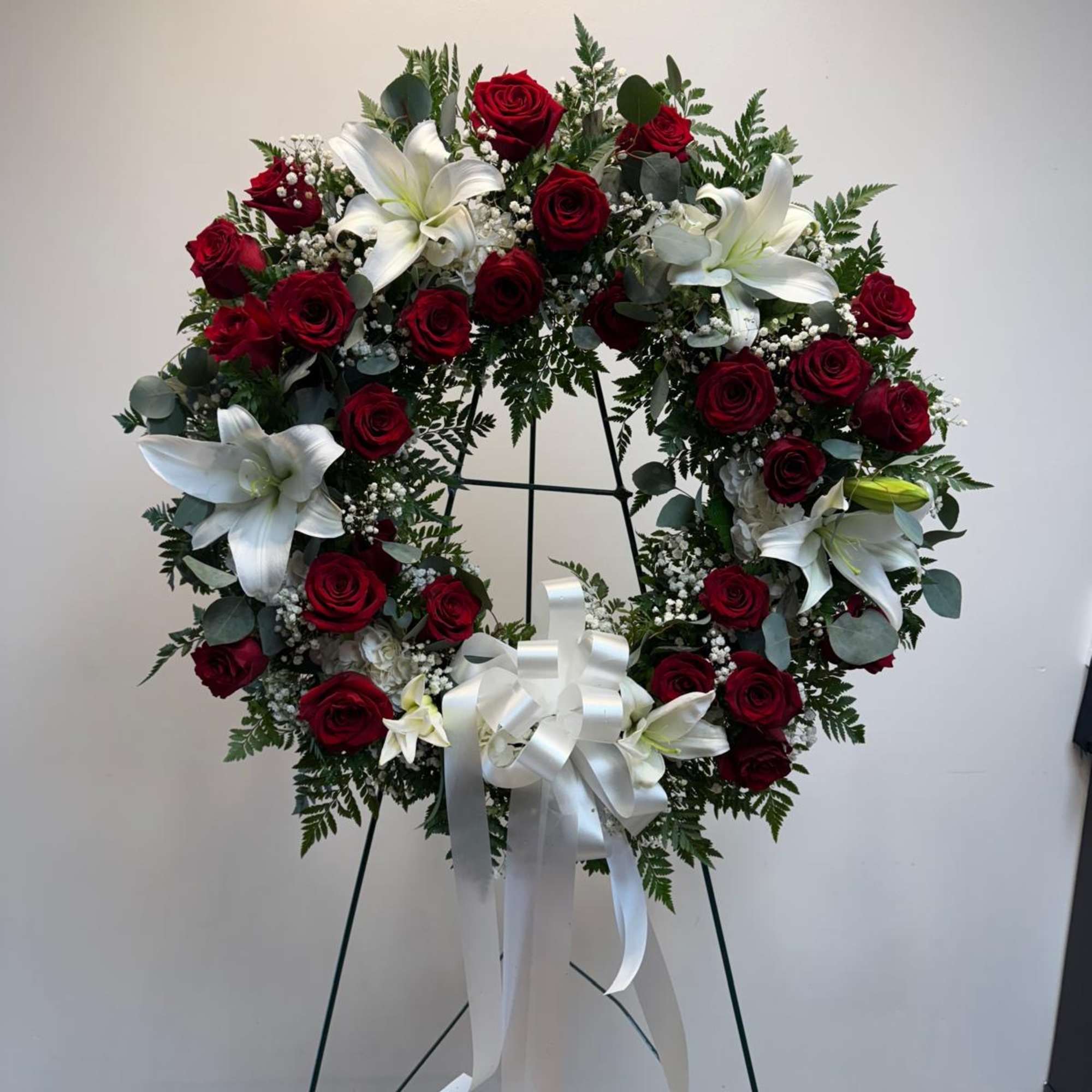 Circular wreath of red roses and white lilies on a stand with a white ribbon bow