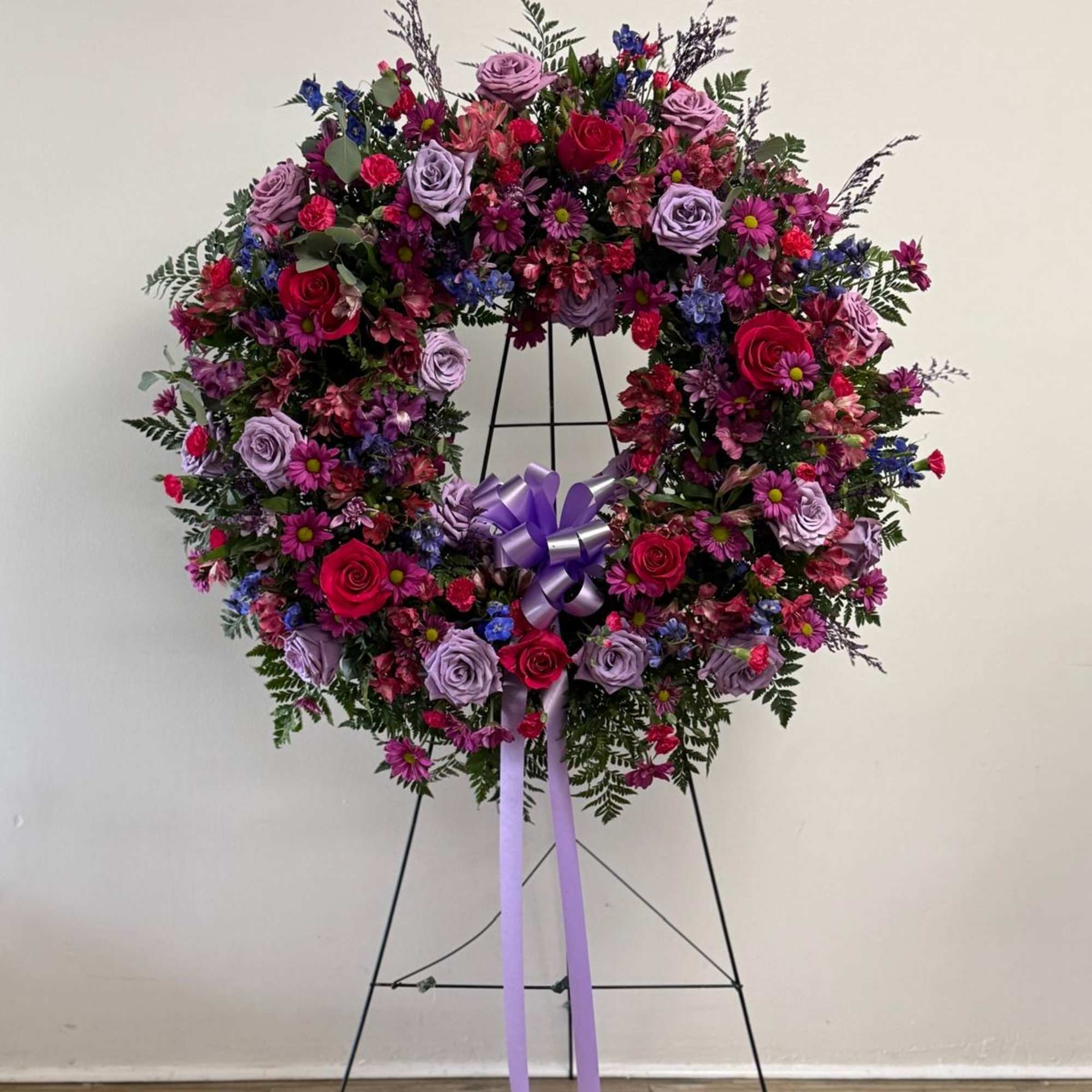 Large floral wreath on a stand with pink, purple, and blue flowers and a lavender ribbon