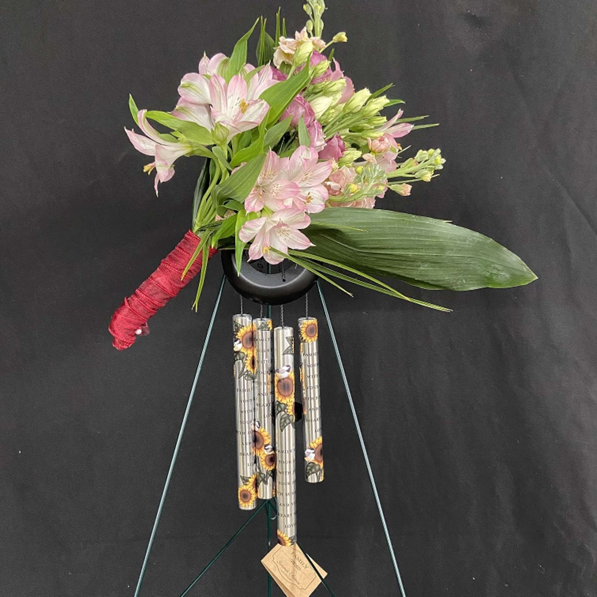 Pink and white flower arrangement with hanging wind chimes on a stand