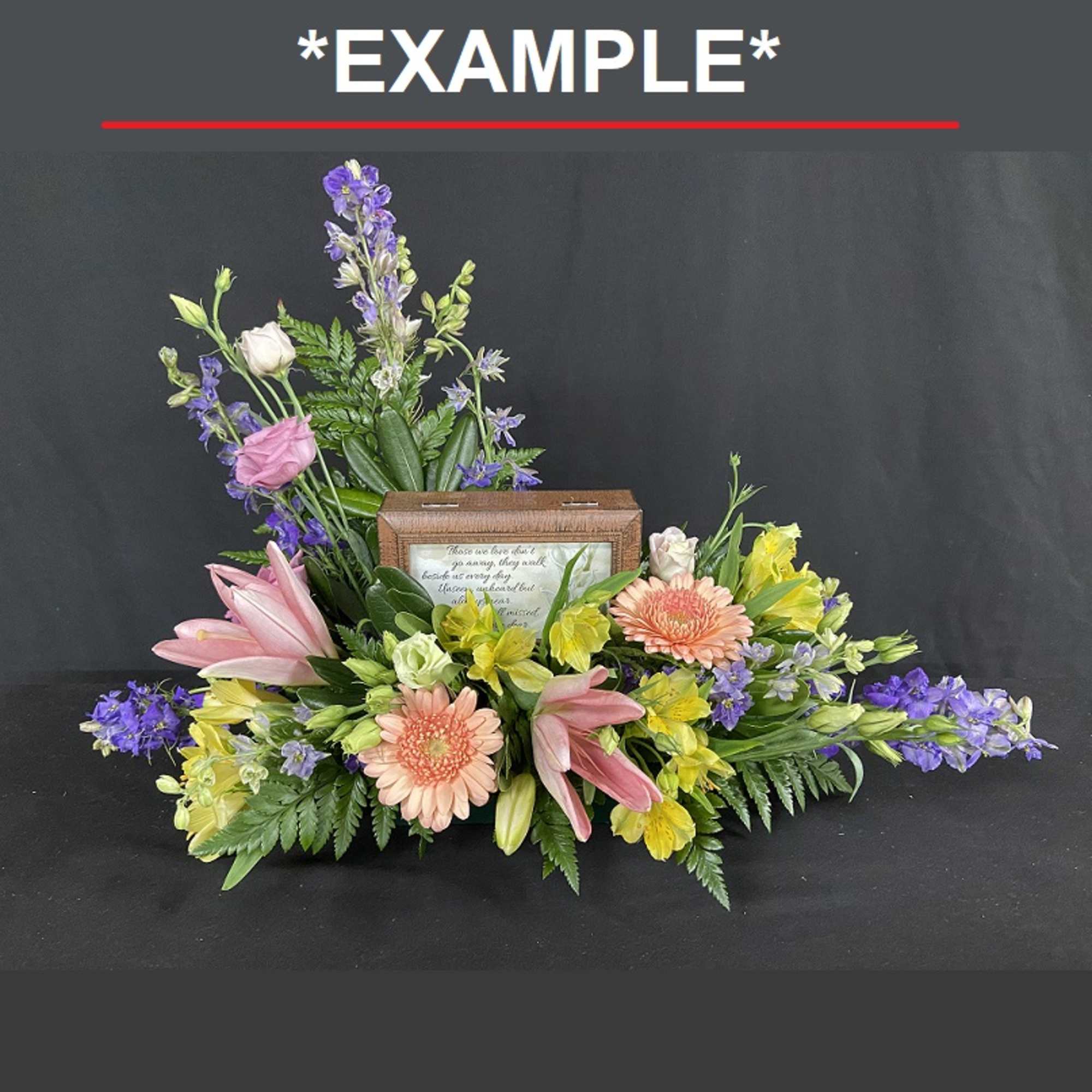 Sympathy floral arrangement with lilies, gerberas, and purple blooms around a framed keepsake