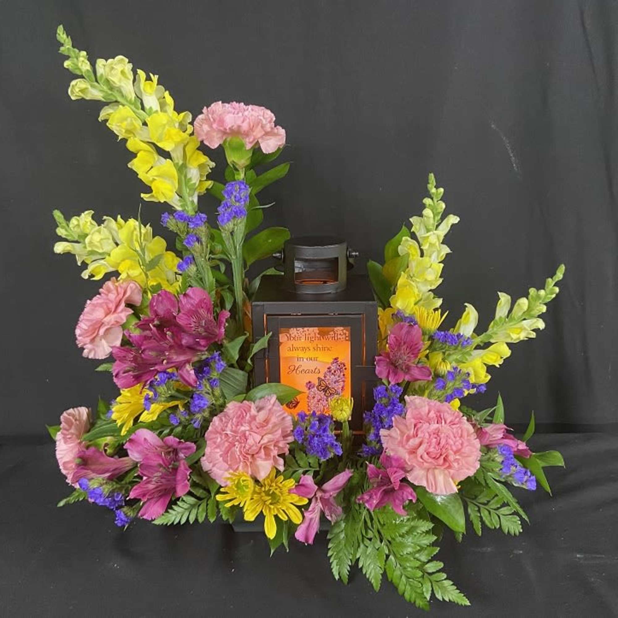 Floral arrangement around a black lantern with pink, yellow, and purple flowers.