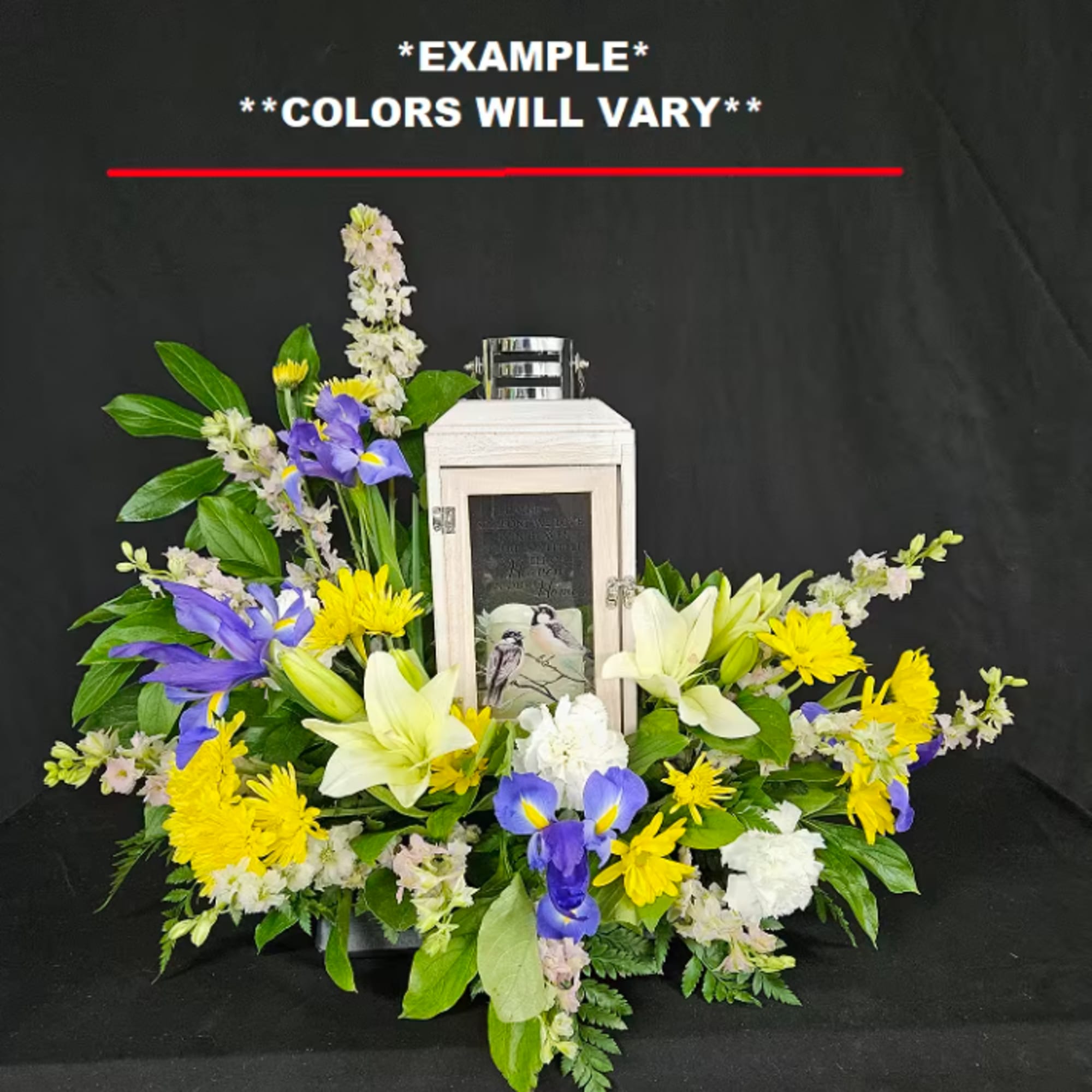 Floral funeral arrangement with lilies, irises, and yellow daisies around a memorial lantern