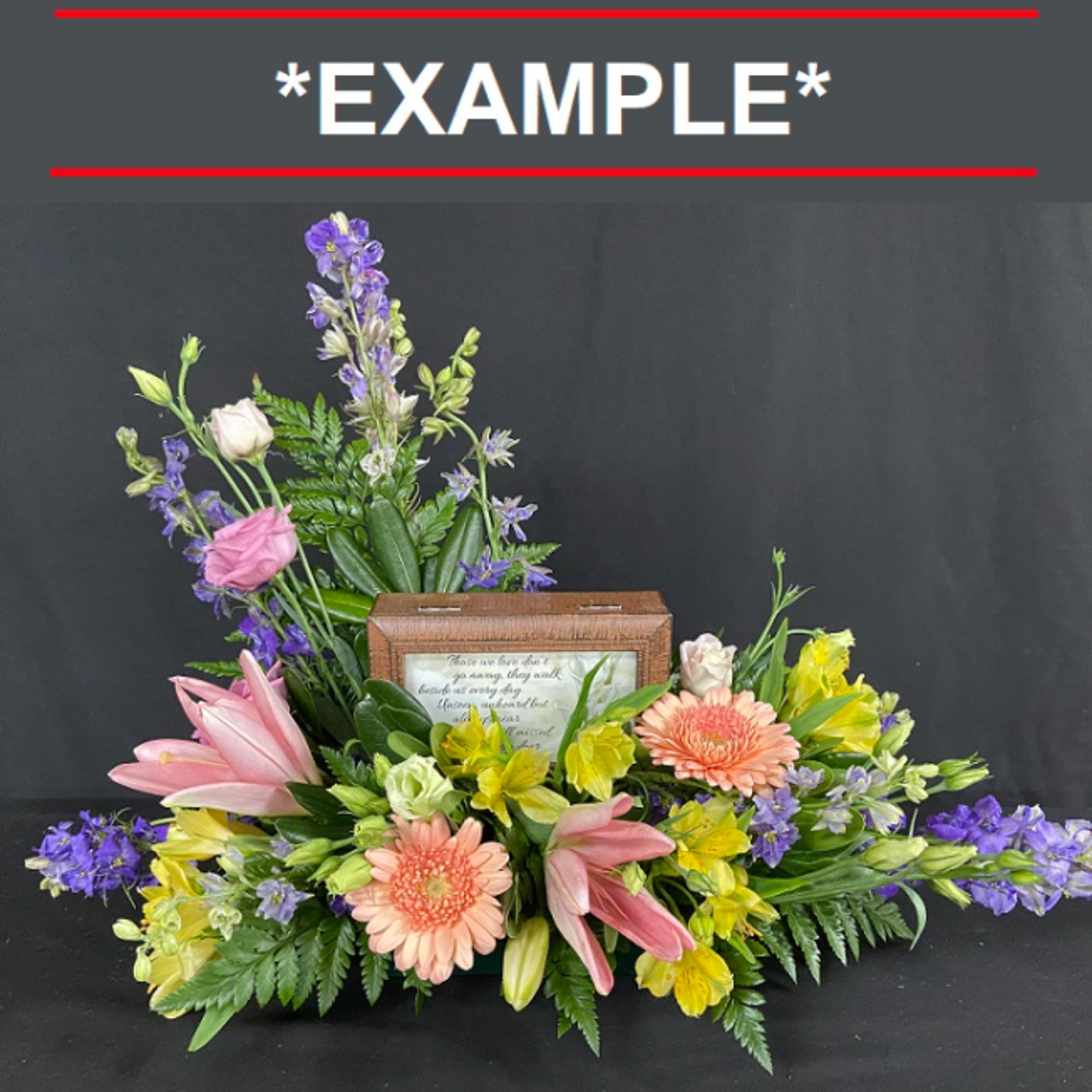 Mixed floral arrangement with pink lilies, gerbera daisies, and purple blooms around a framed plaque