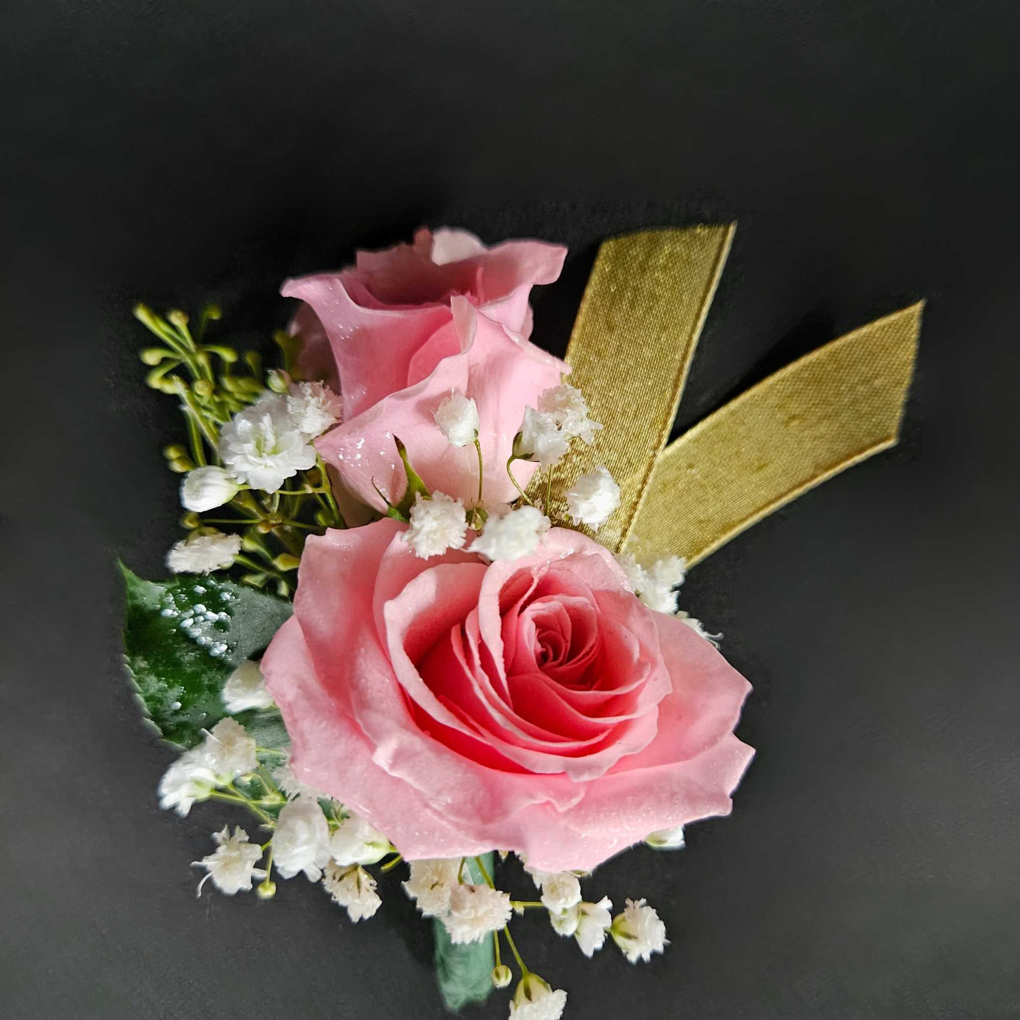 Pink rose and white accent flower corsage with a gold ribbon on a dark background
