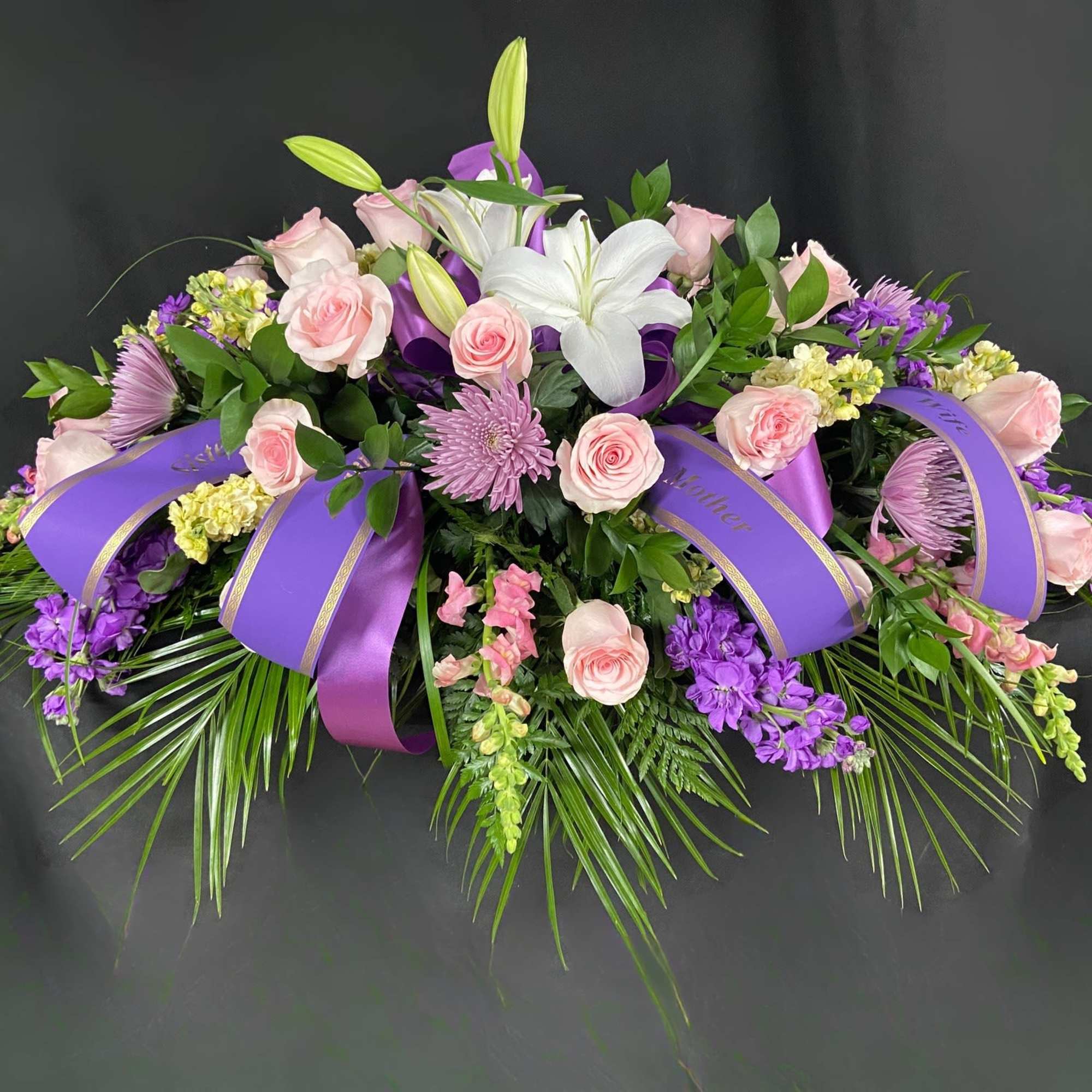 Pink roses and white lilies arranged with purple ribbons.