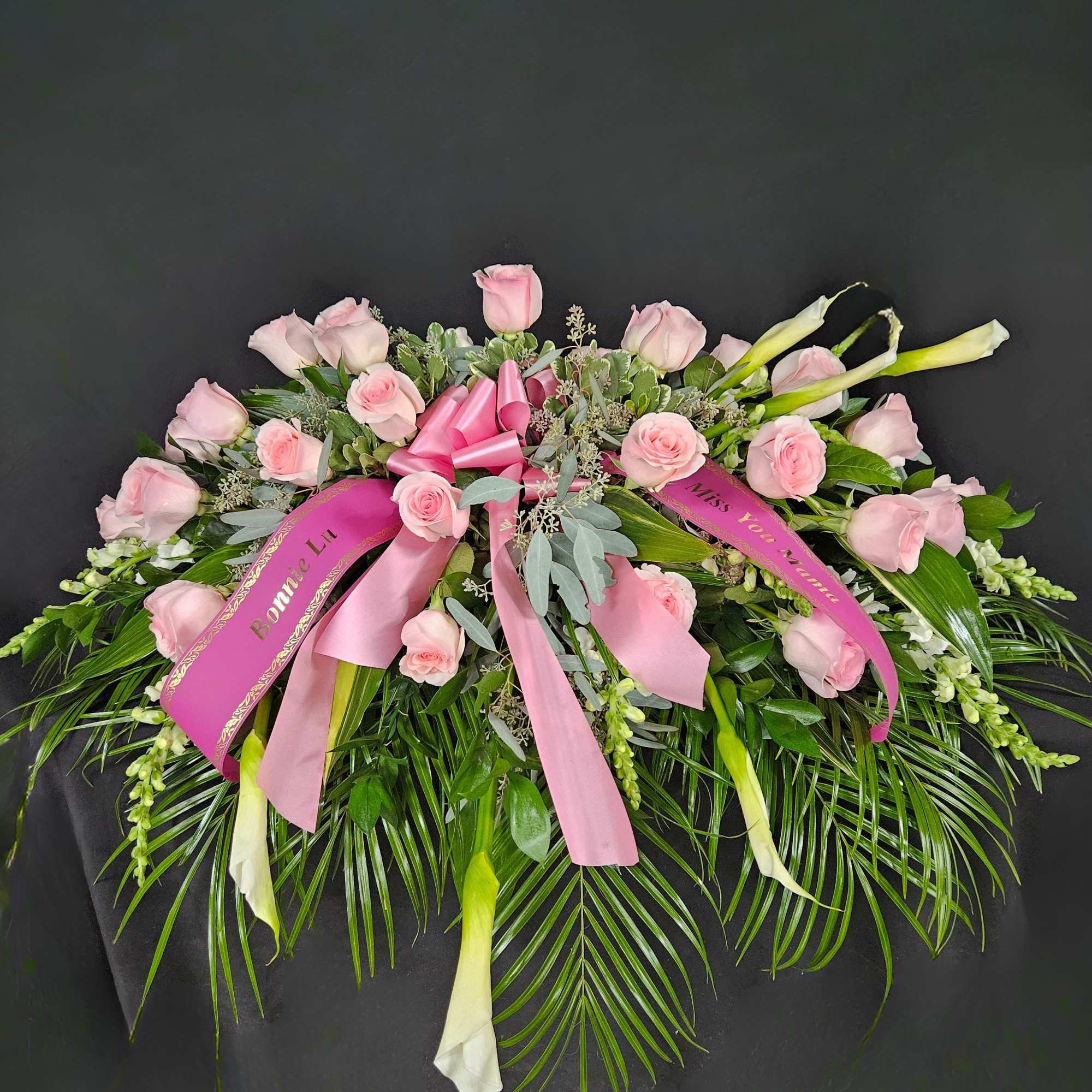 Pink roses and white calla lilies arranged with ribbons on a black background.
