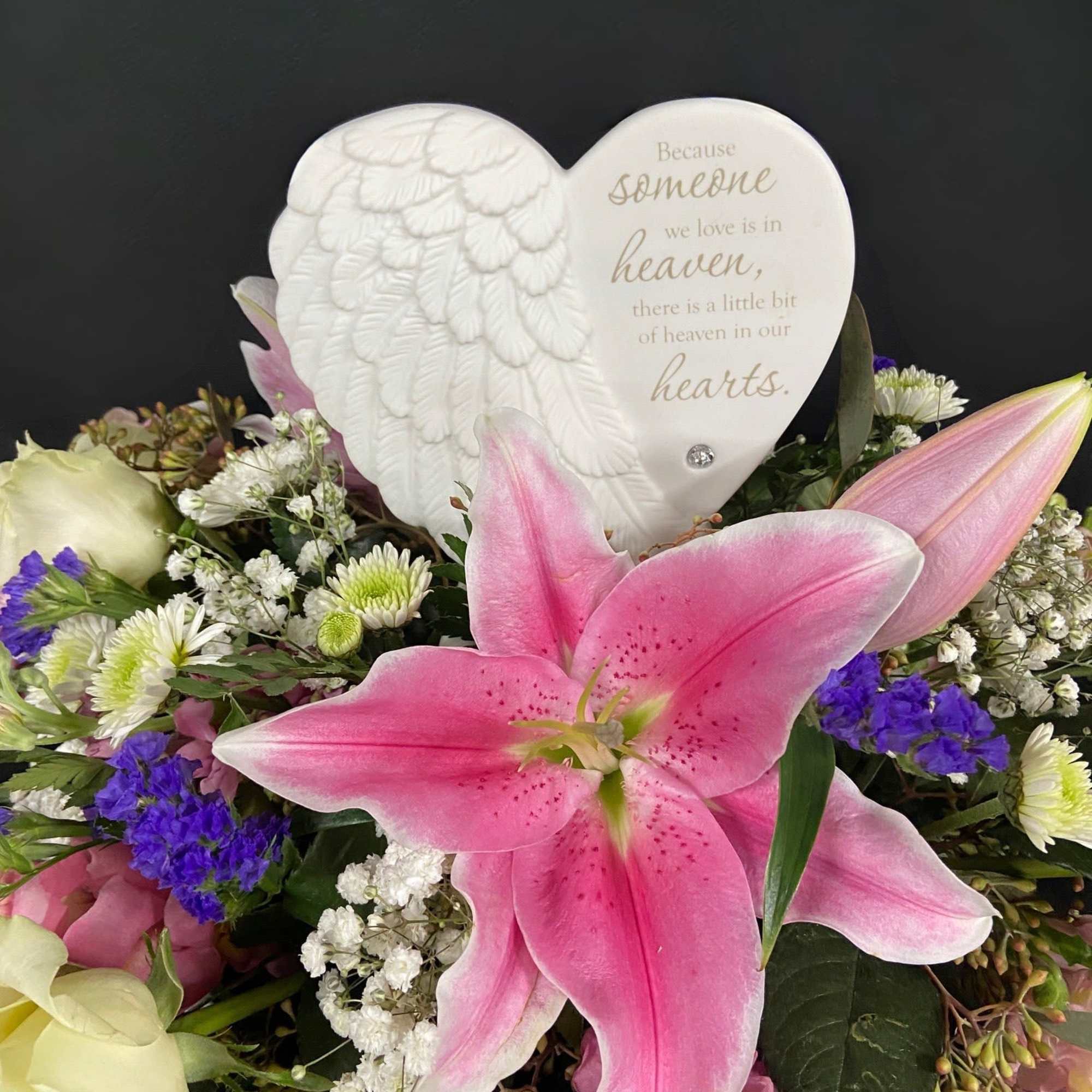 Pink lilies and white roses surround a heart-shaped memorial plaque.