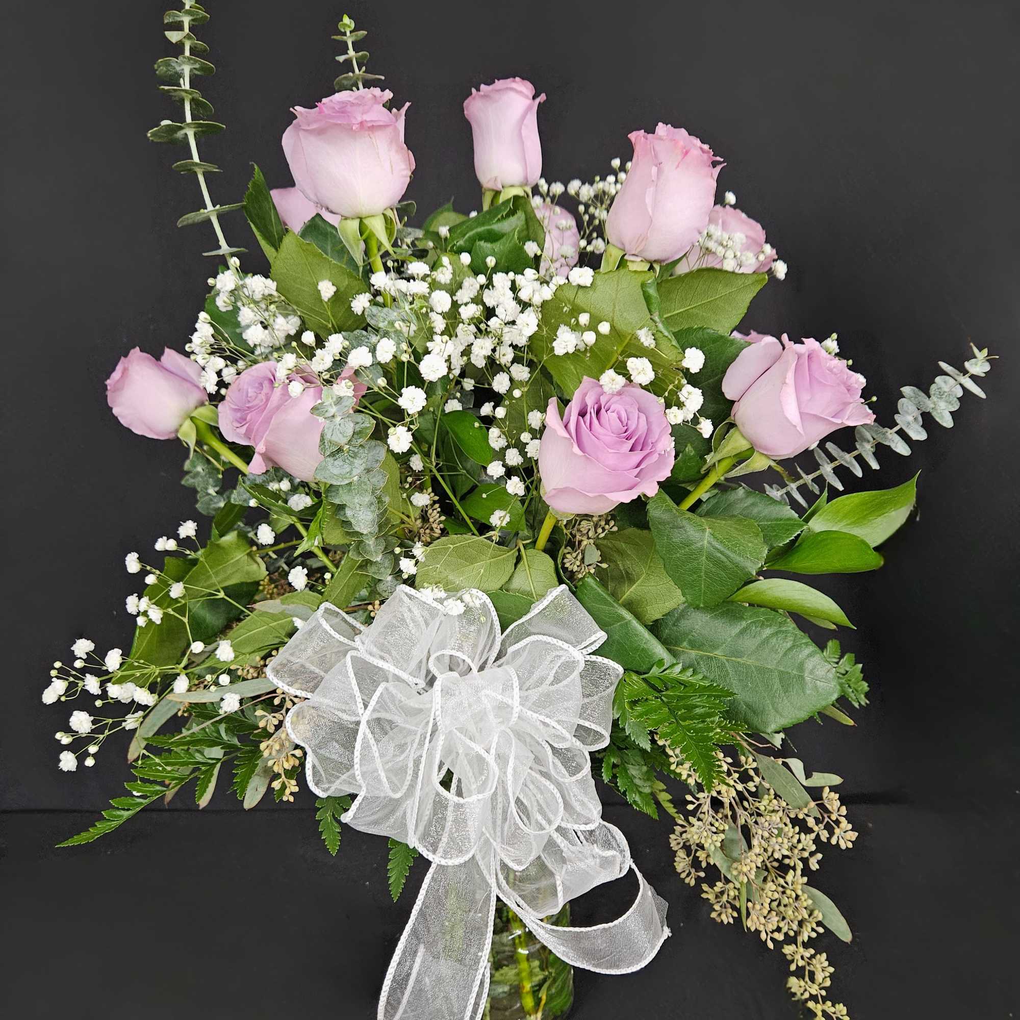 Pink roses and baby's breath in a glass vase with a white bow