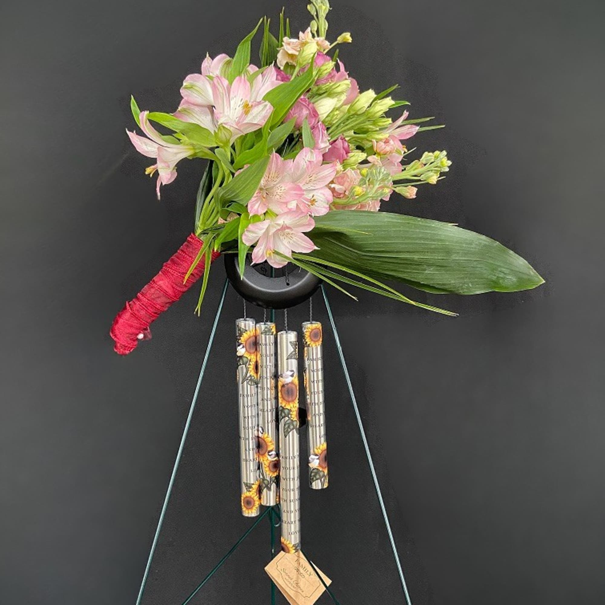 Pink and white flowers arranged in a hanging display with a red-wrapped handle