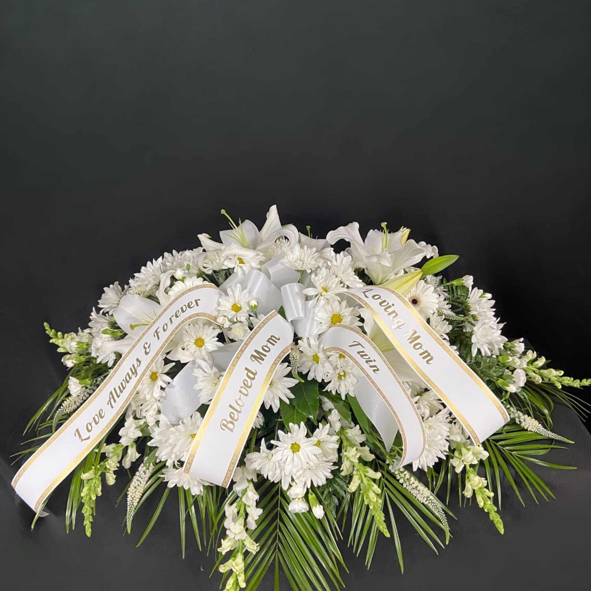 A bed of beautiful greenery is covered with white daisy poms and