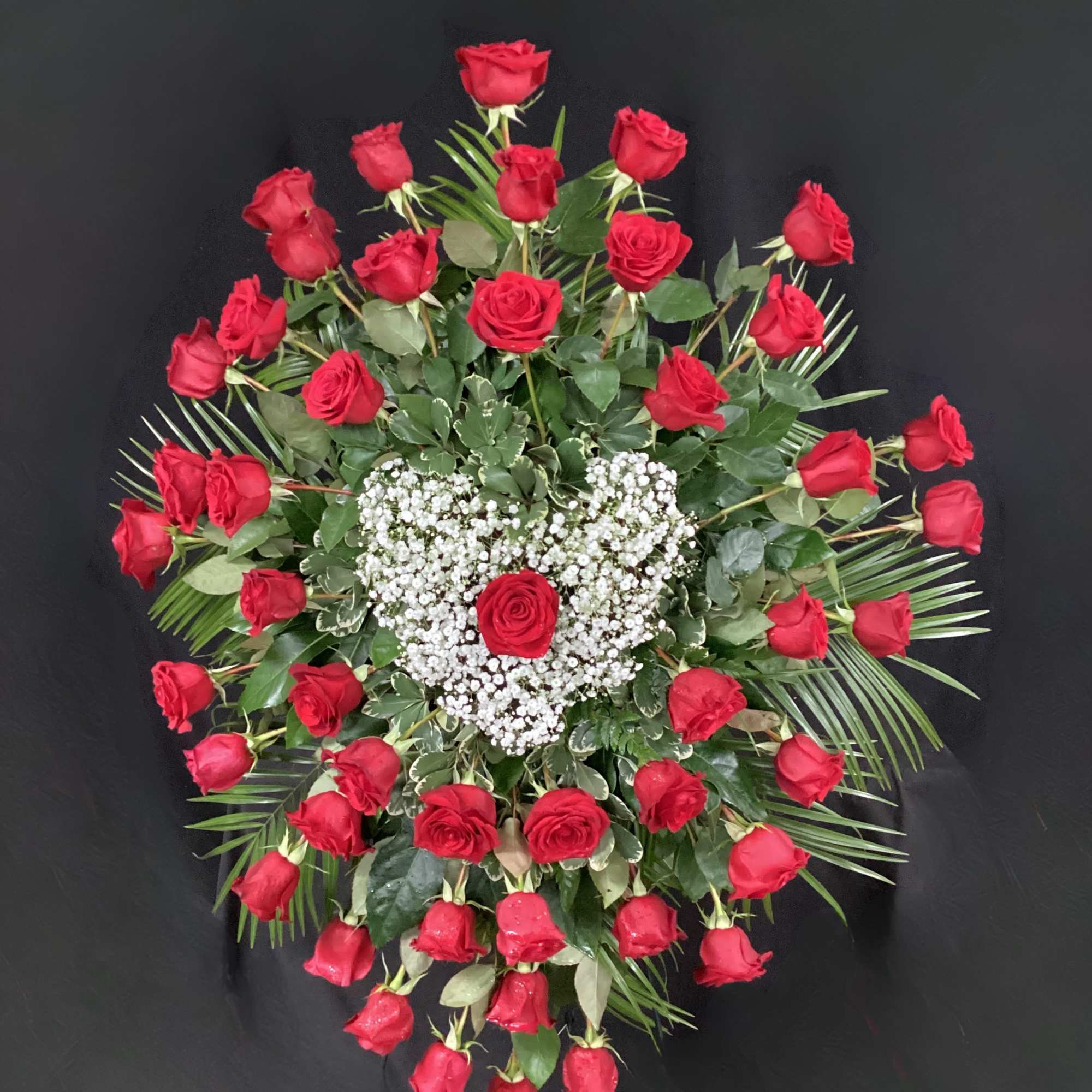 Heart-shaped red rose arrangement with baby's breath on a black background