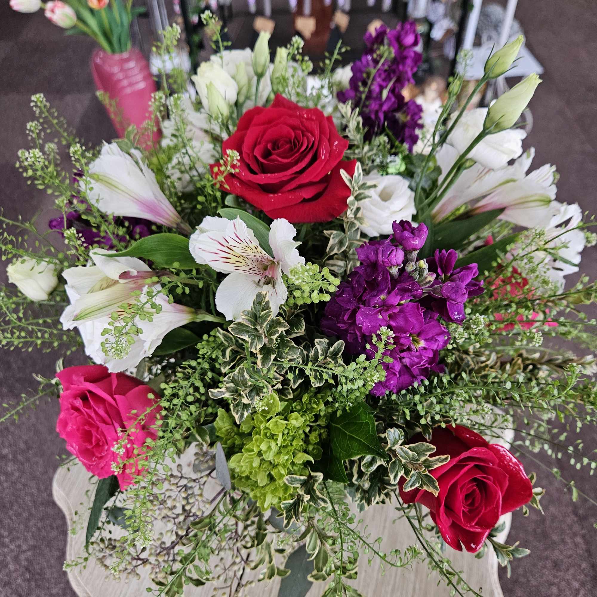 Mixed bouquet of red roses, white alstroemeria, and purple flowers in a lush arrangement on a small table