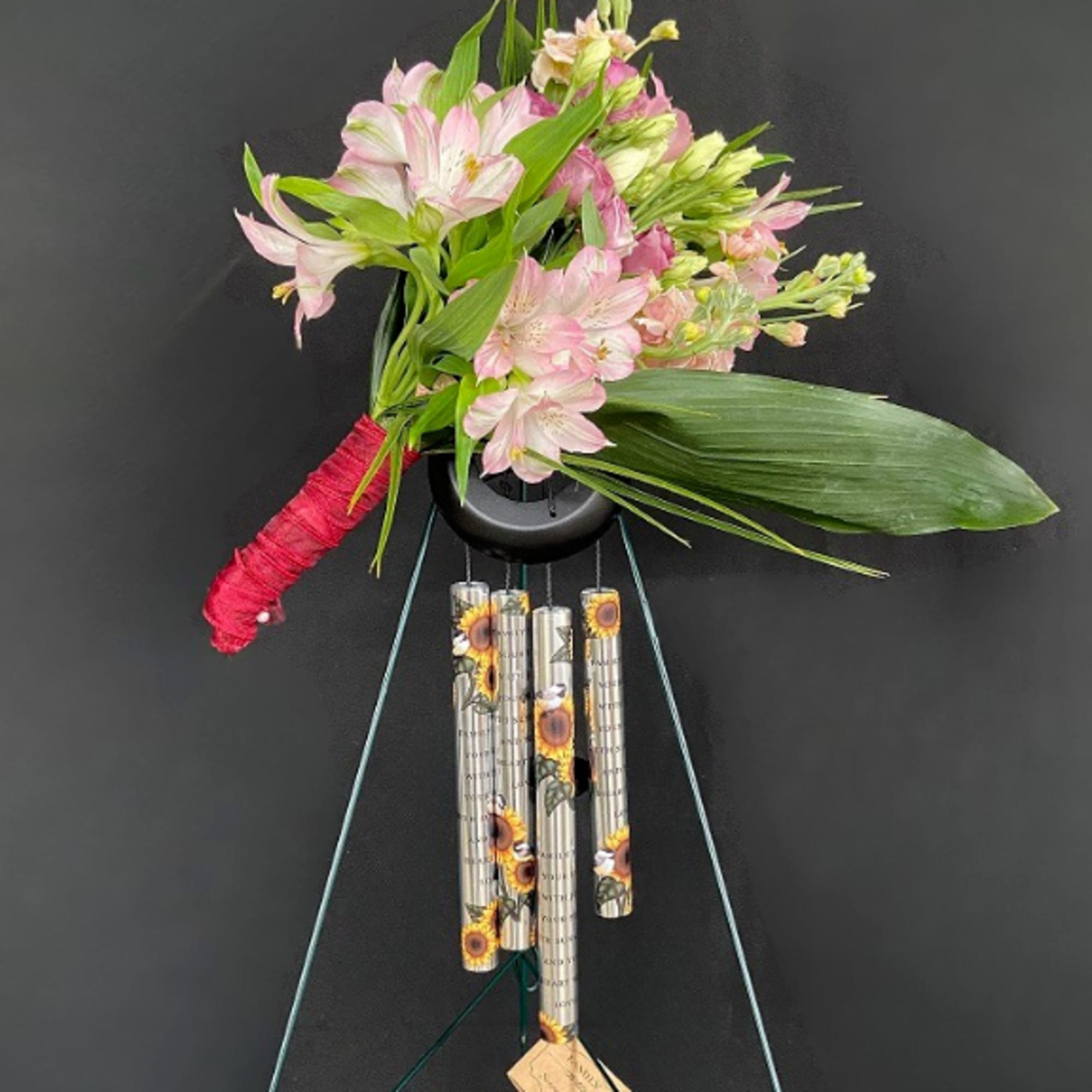 Pink alstroemeria bouquet tied to sunflower wind chimes on a tall metal stand.