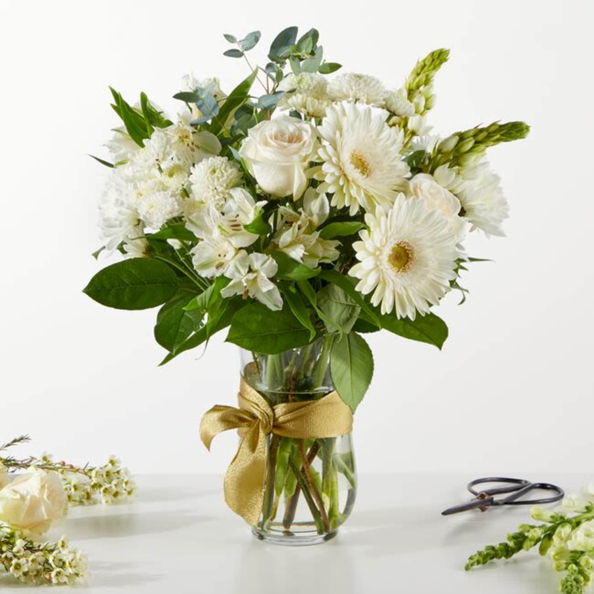 White flower bouquet in a glass vase with a gold ribbon