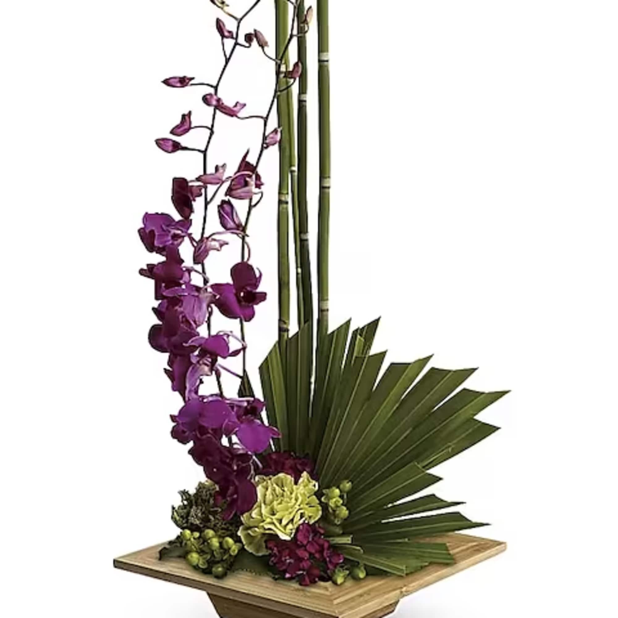 Tall floral arrangement with purple orchids and green tropical leaves in a wooden base