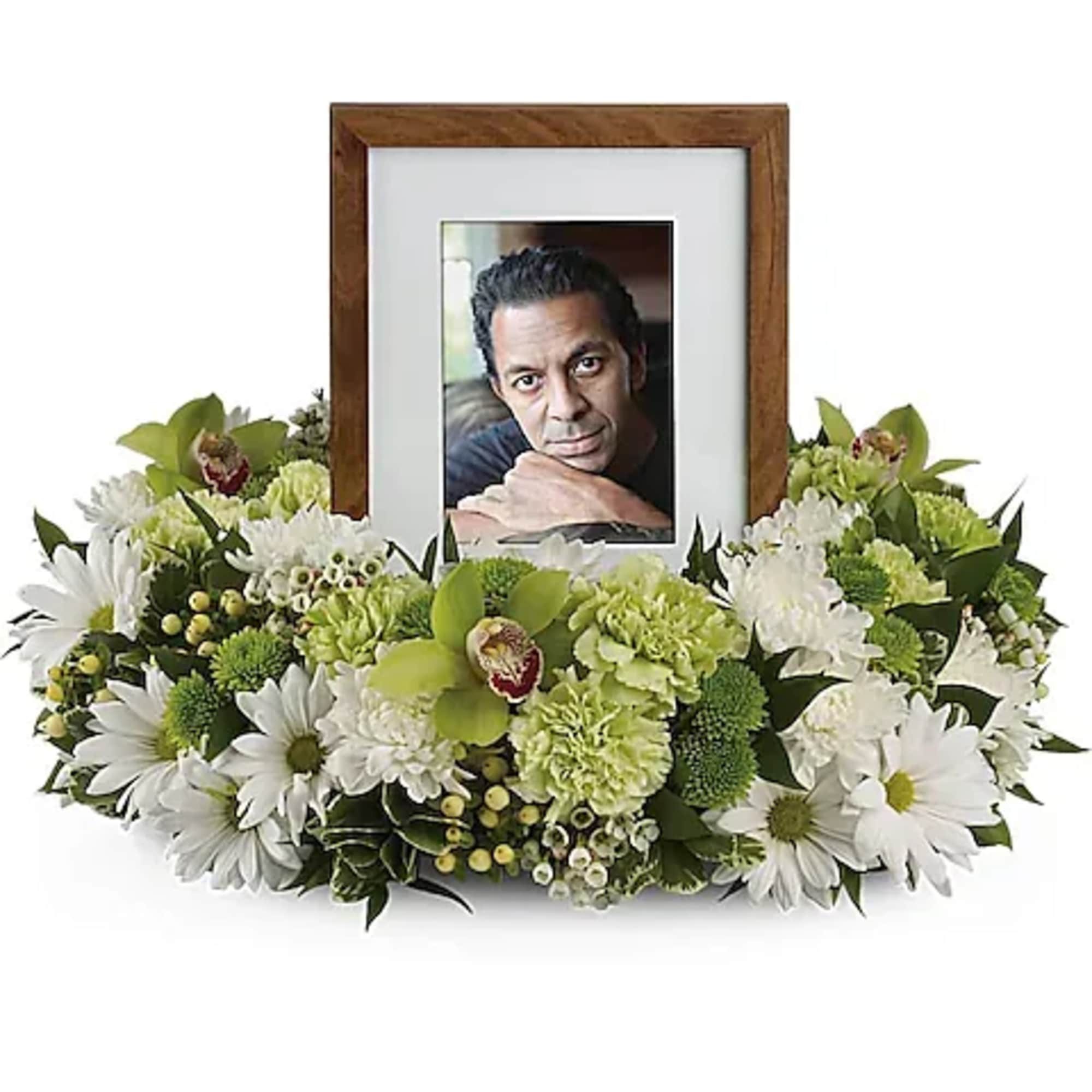 Framed photo surrounded by white and green funeral flowers