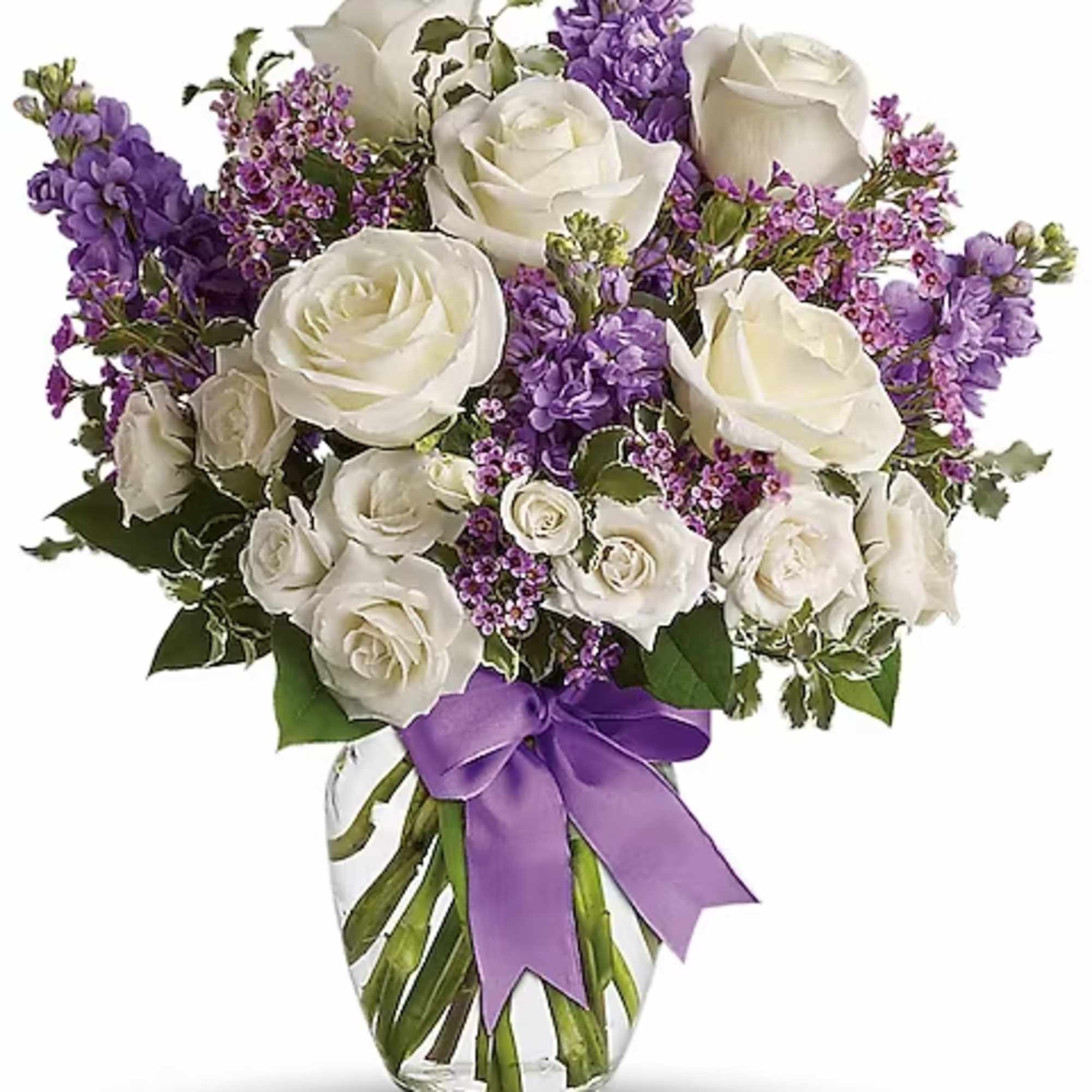 Vase of white roses and purple flowers with a lavender ribbon bow around a clear glass vase