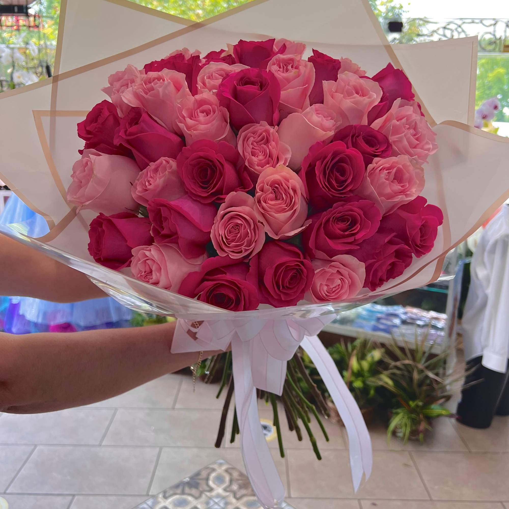 Hand-tied bouquet of hot pink and light pink roses wrapped in white paper with ribbon
